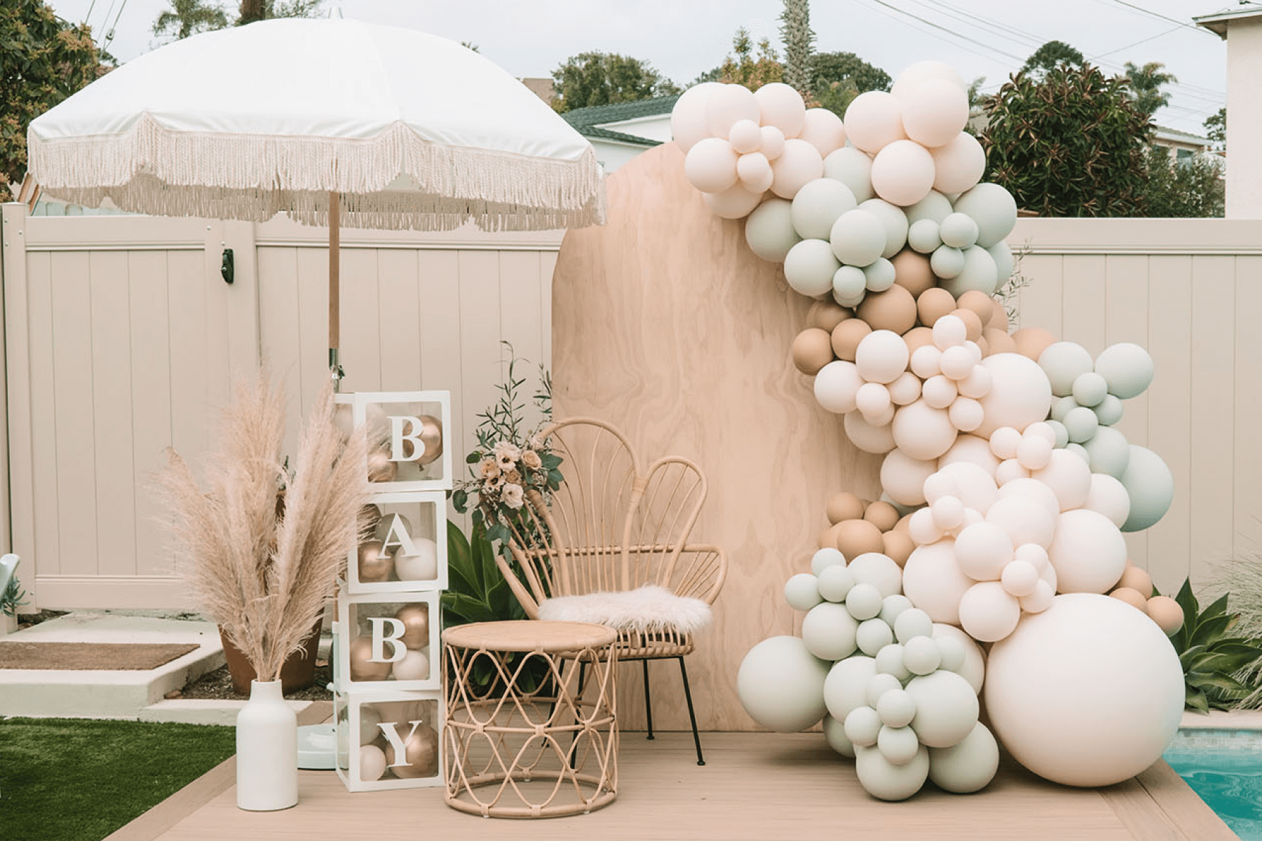 A pastel balloon installation with a pool umbrella, rattan chair, and decorative BABY blocks.