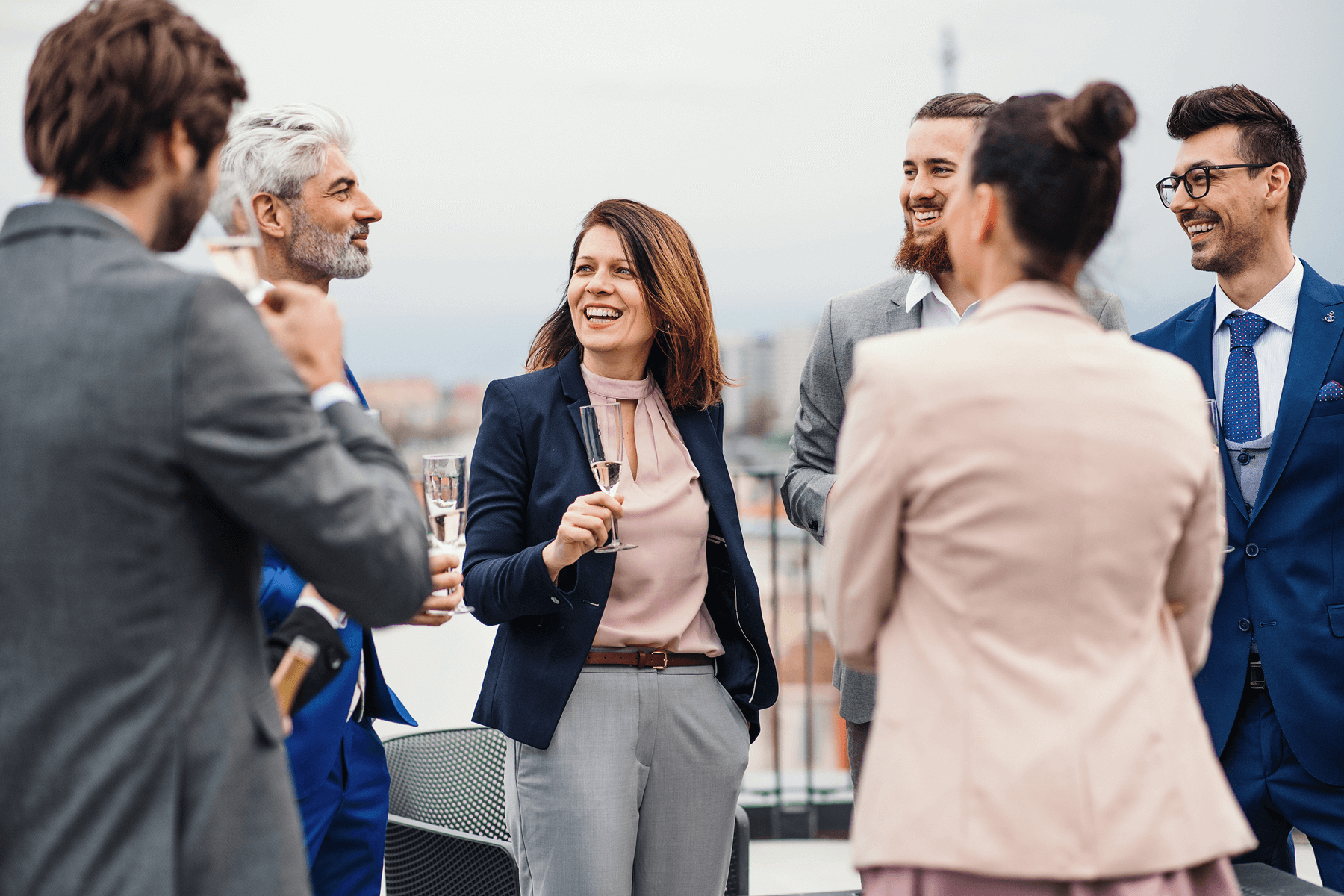 People in business attire hold drinks on a rooftop.