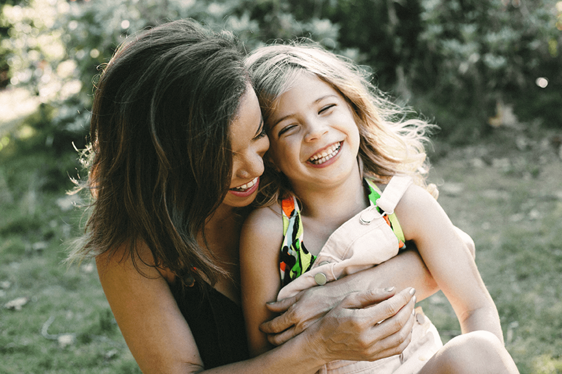 A woman embraces a young child outdoors, smiling.