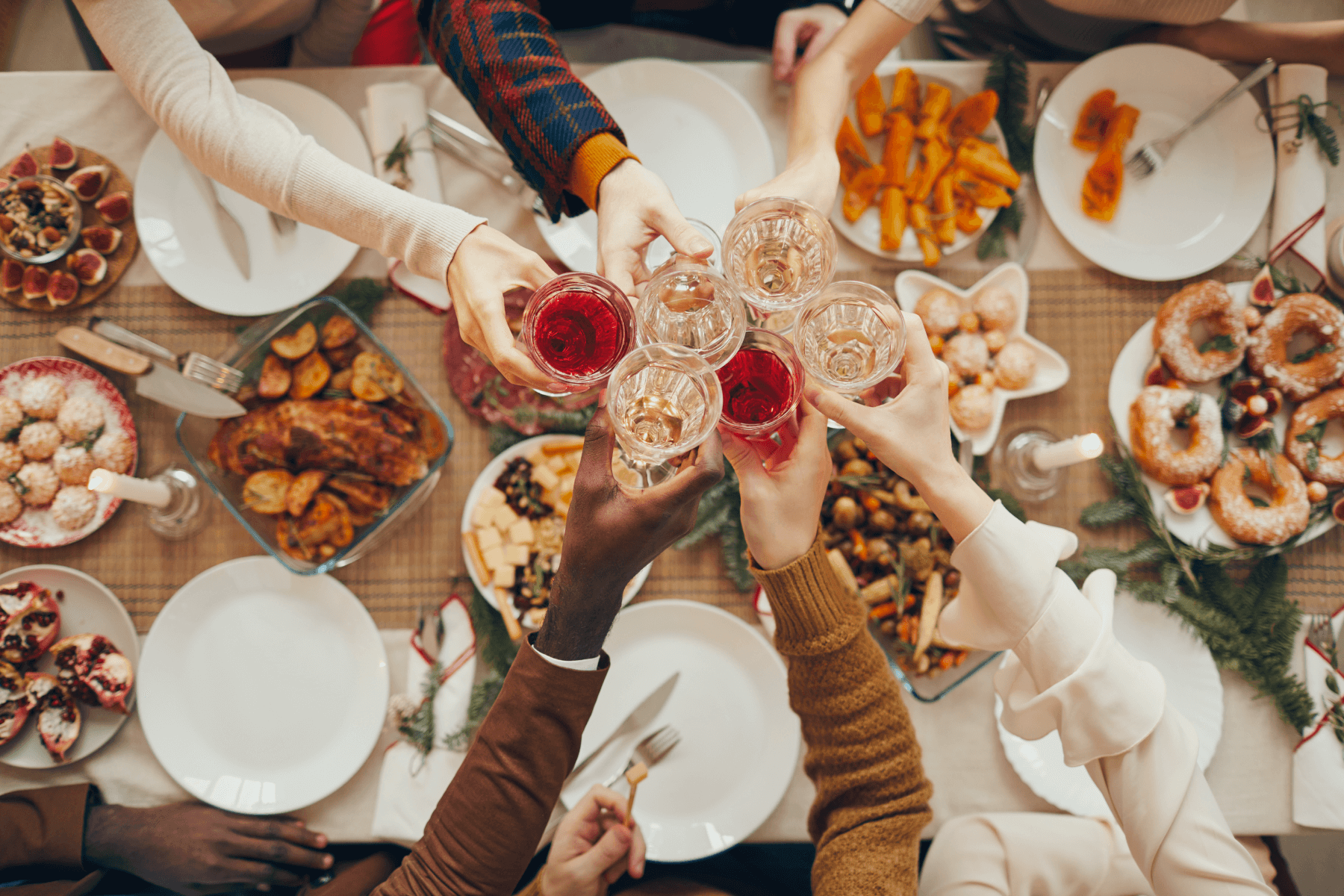 Hands holding drinks and doing cheers over a table full of holiday appetizers.