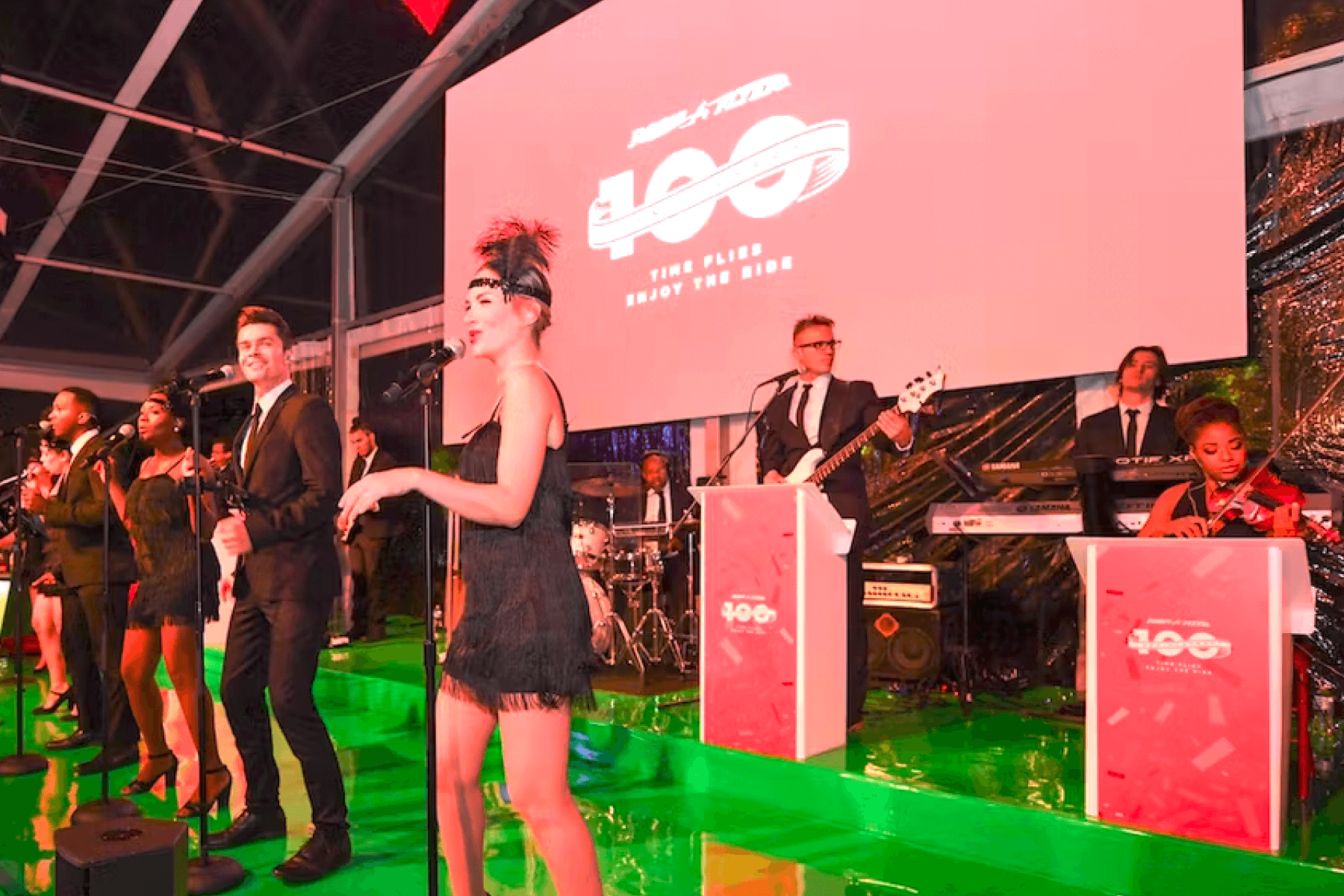 Women and men in black-tie and flapper attire perform a musical number on stage.