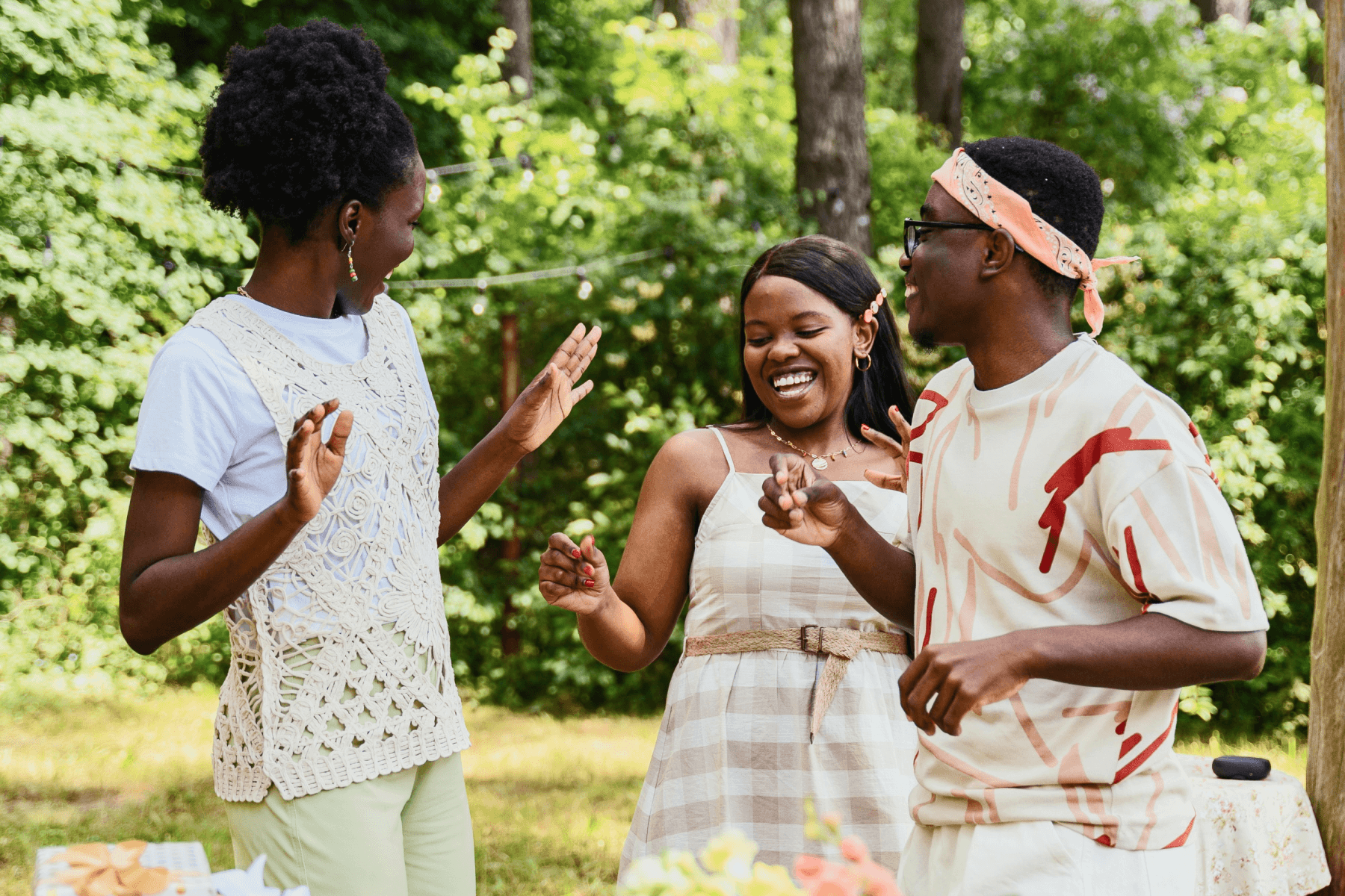 three people in warm-weather clothing smile in a green outdoor setting