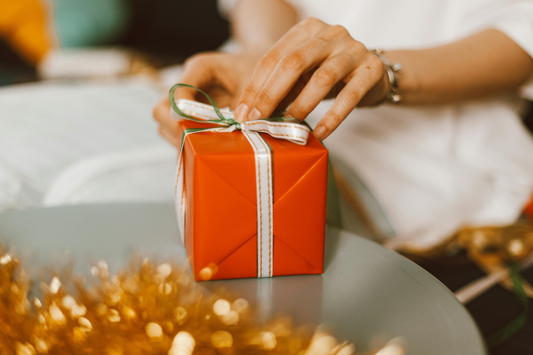 Hands opening a small gift wrapped in red ribbon.