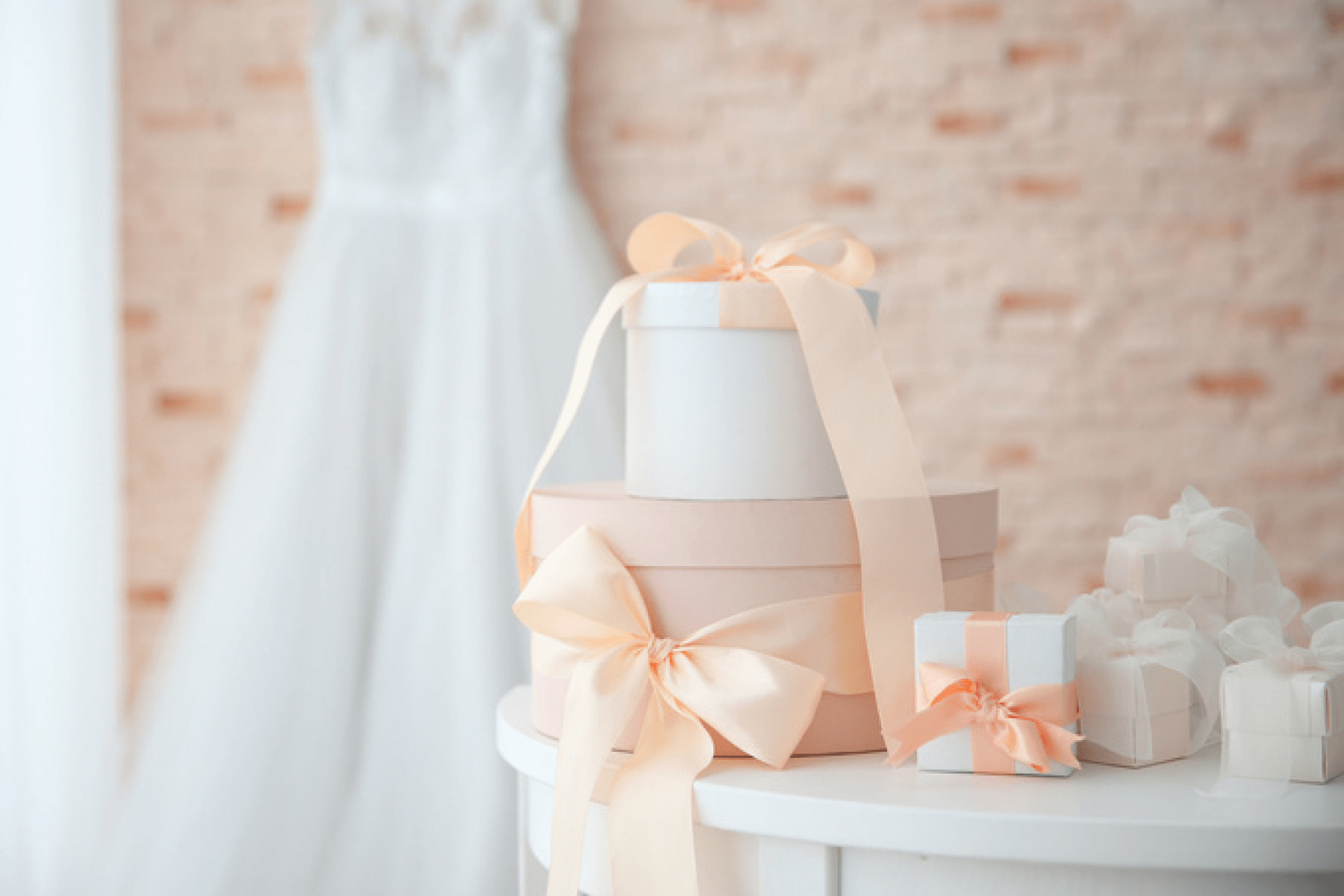A white table with wrapped pink and white gifts with a wedding dress hanging in the background.