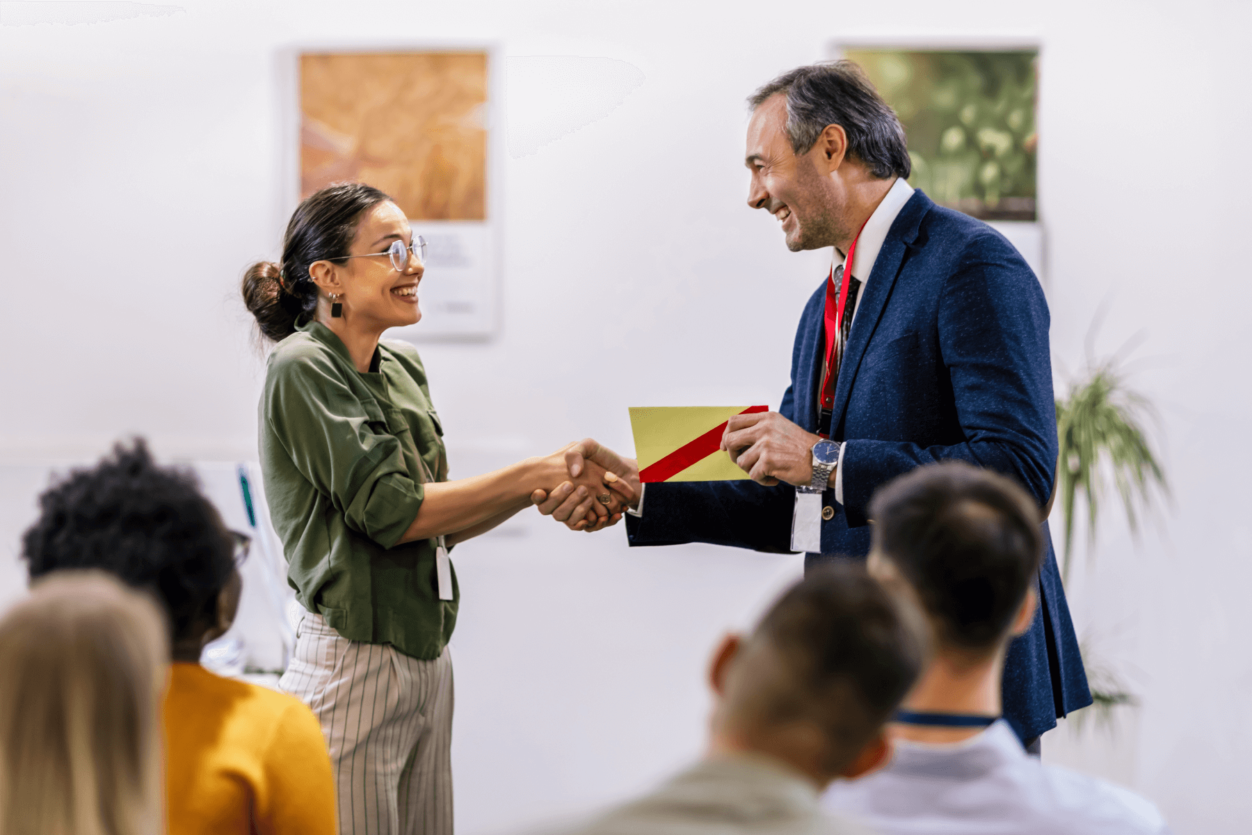 A man and a woman in business clothes standing in front of a seated group shaking hands.