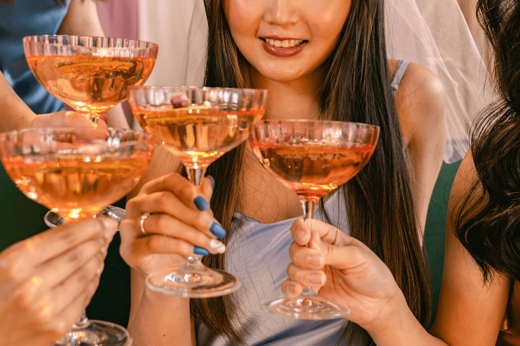 Close-up of four women’s hands holding cocktail glasses.