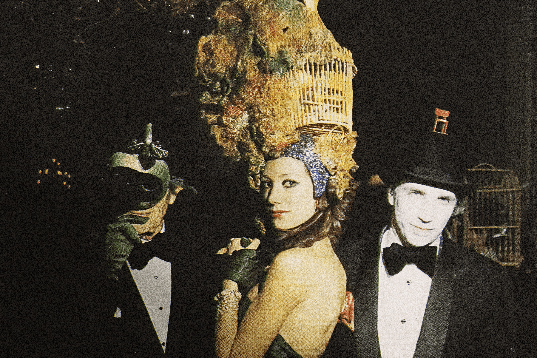 A photo of two men and one woman at a masquerade party, one man wearing a mask, the woman has an elaborate headpiece in gold, and the other man wearing a tuxedo and black hat.