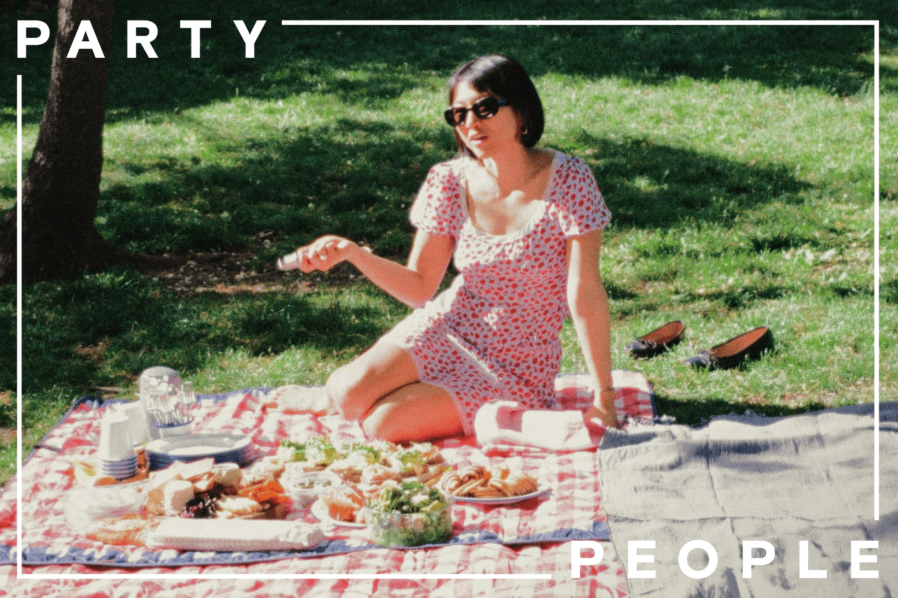 ALT: Inside a frame with text reading, ‘Party People’, Sue Chan sits on a red and white picnic blanket alongside a spread of snacks, plates, and cups. Beside her is a separate grey blanket. In the background, two black shoes sit on green grass. 