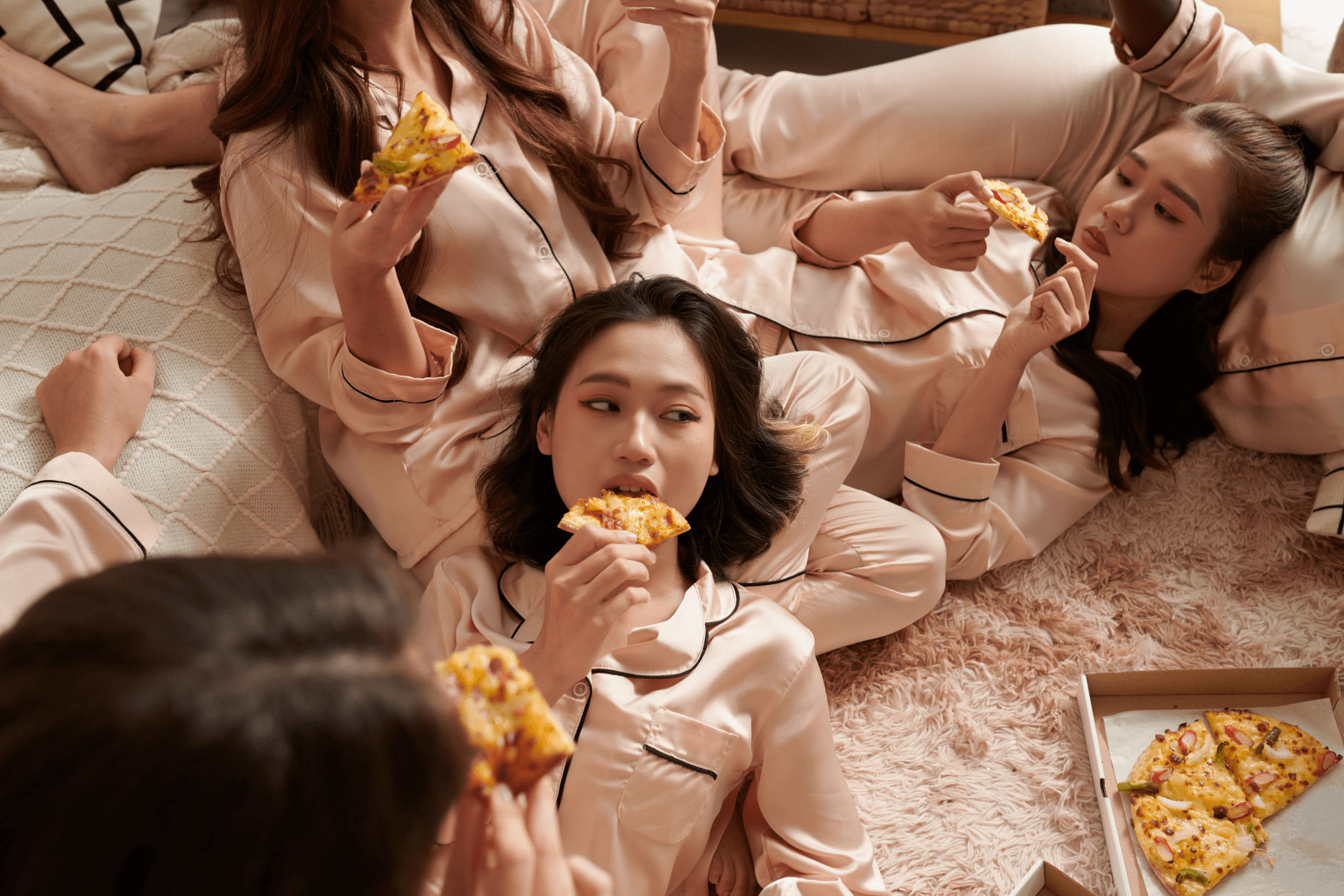 Girls in matching PJs sitting on the floor eating pizza.