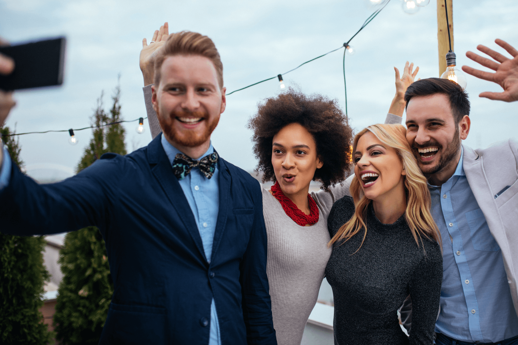 Two men and two women in suit jackets and business casual attire pose for a selfie at an outdoor event.