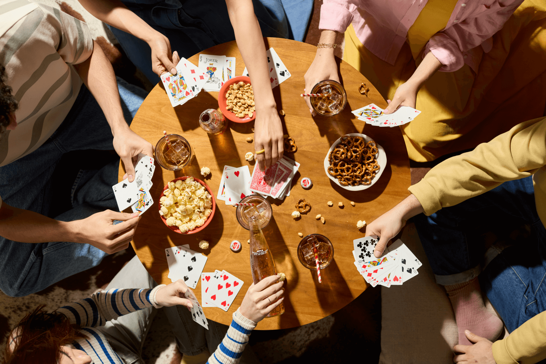 An overheat shot of a table filled with snacks, drinks, and people playing cards.