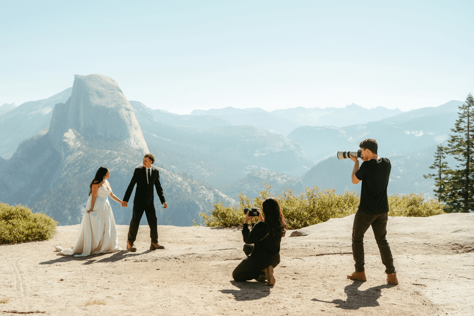 Two photographers taking photos of a bride and groom in front of a mountain.