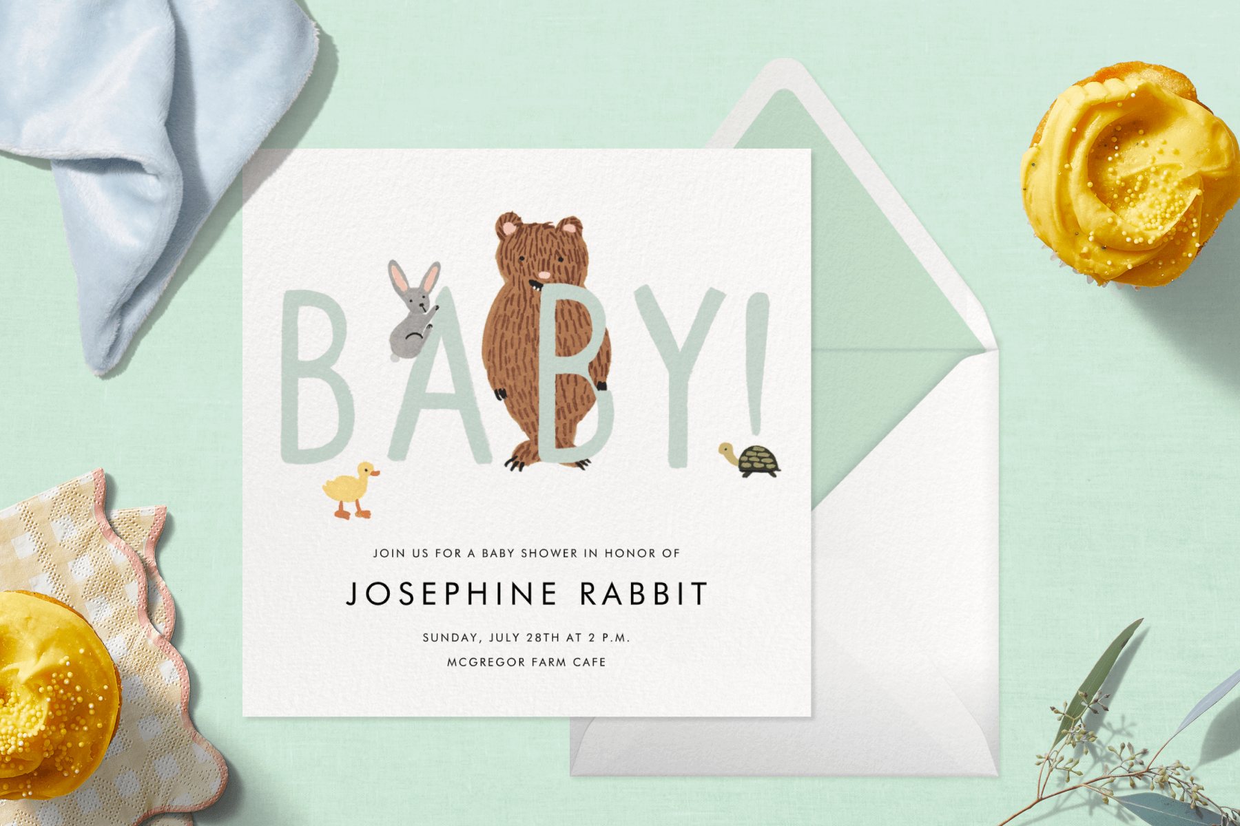 An invitation with a duckling, rabbit, bear, and turtle and the word BABY! surrounded by yellow cupcakes and napkins.