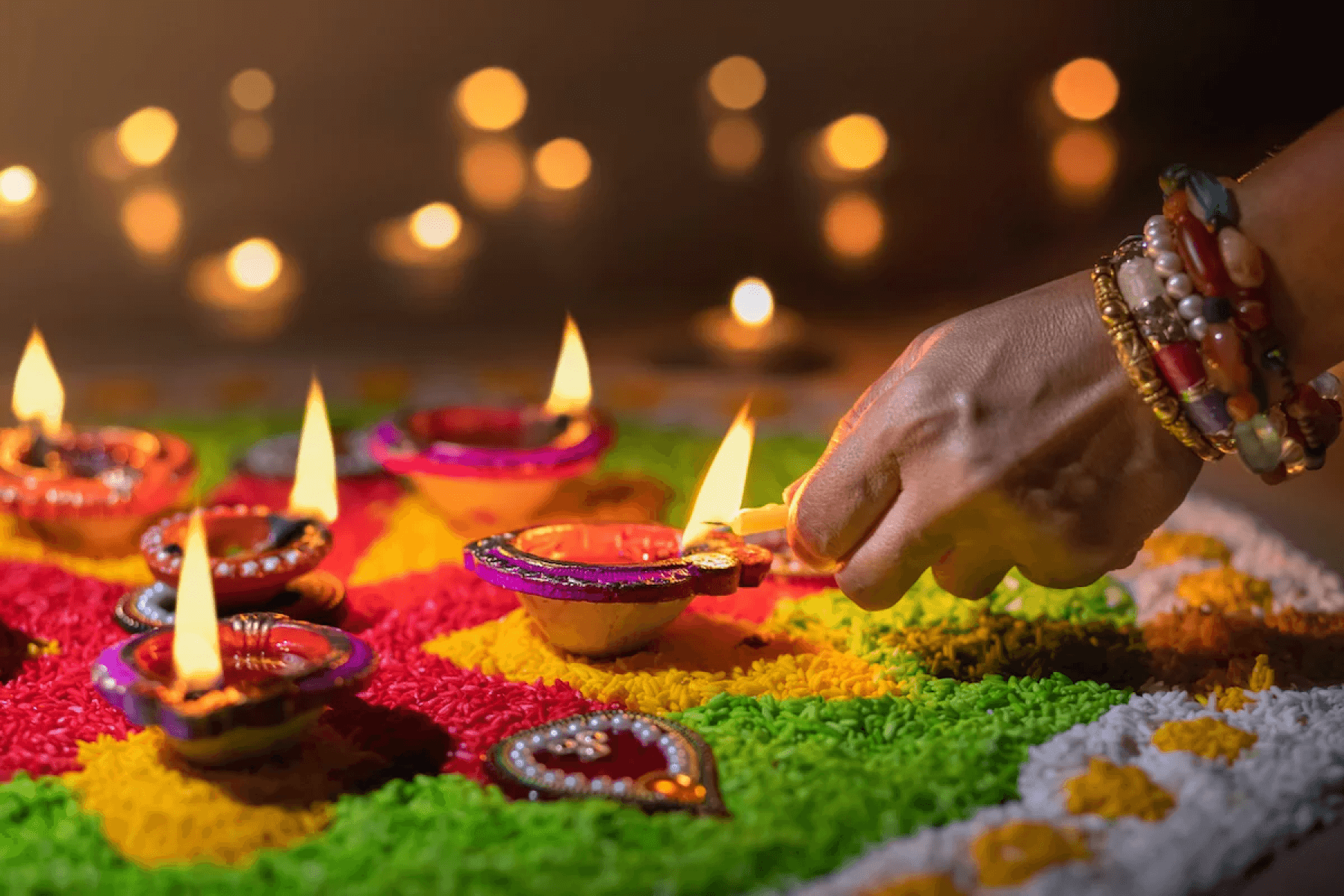 A woman’s hand lighting a diya in a rangoli decoration.