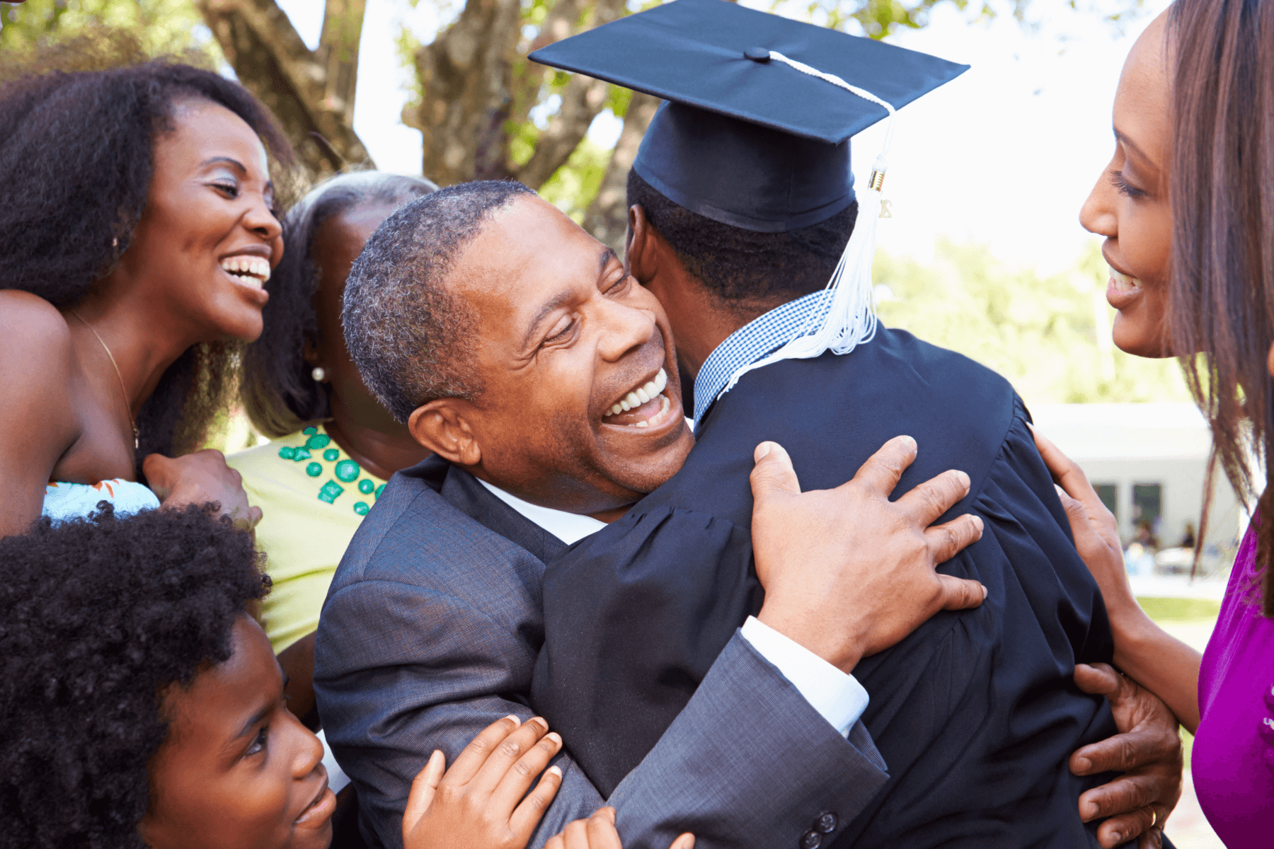 A man hugs someone in a cap and gown as family looks on smiling