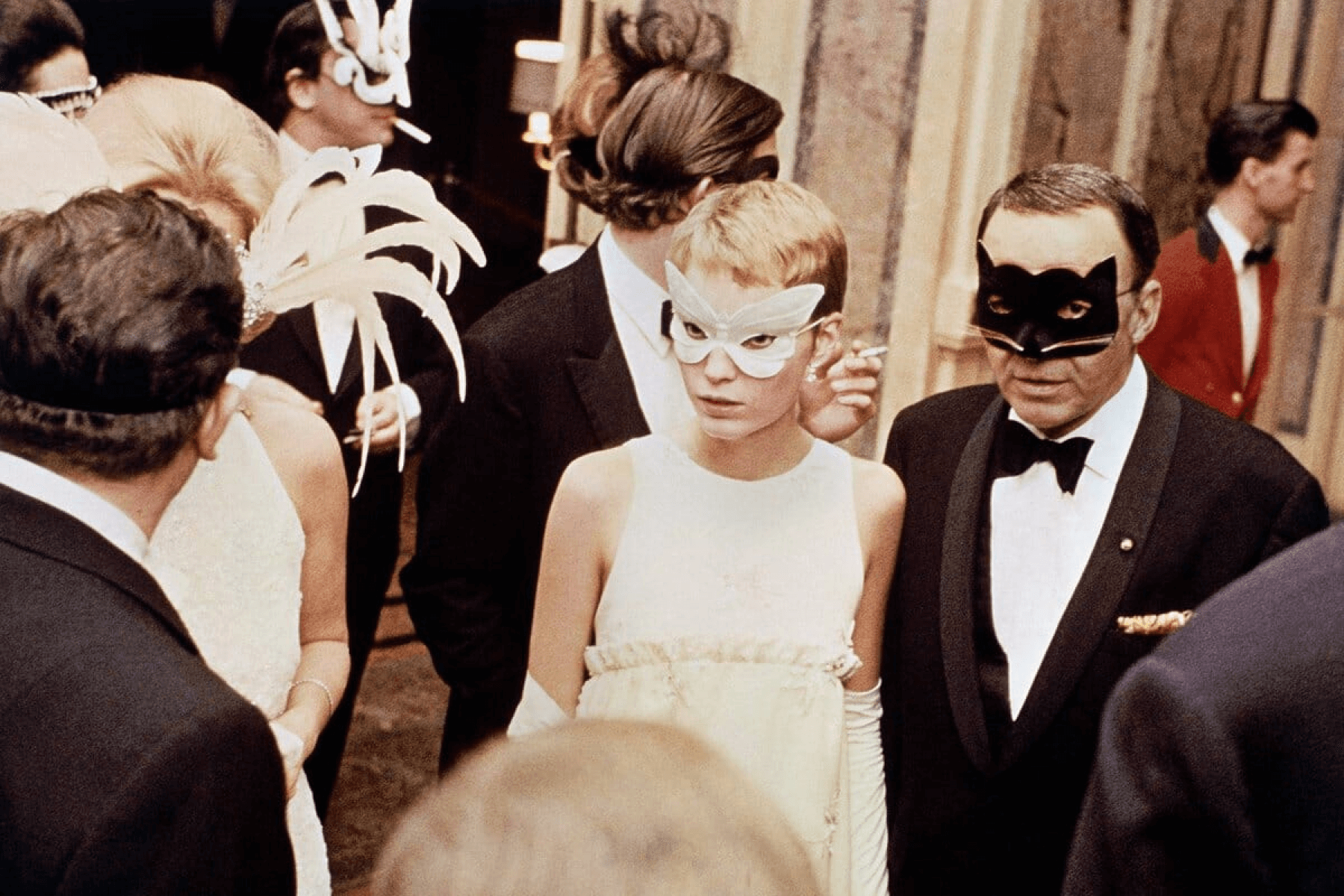 A vintage photograph of Mia Farrow and Frank Sinatra wearing masks and formalwear at a masquerade ball.
