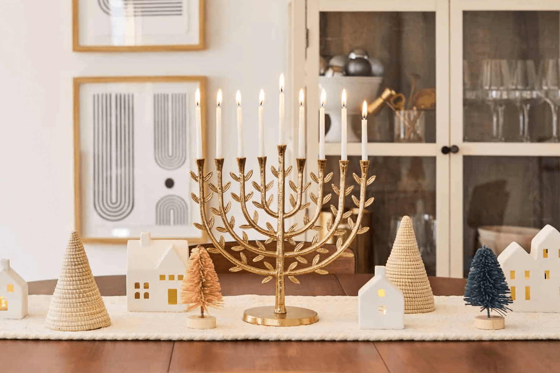 A gold Chanukkiah with leaf details is lit for the 8th night of Hanukkah on a table with winter-themed ornaments.