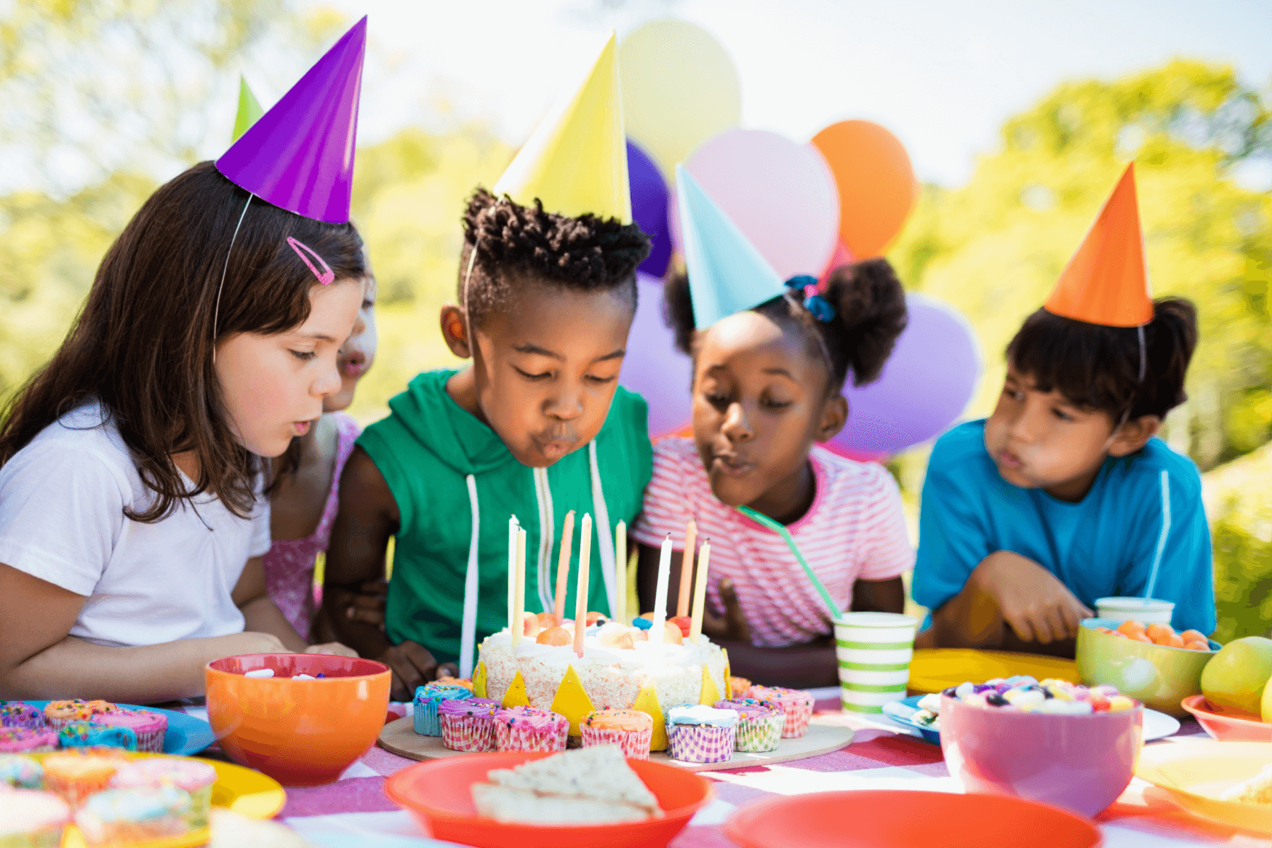 Kids in colorful party hats blow out birthday candles.