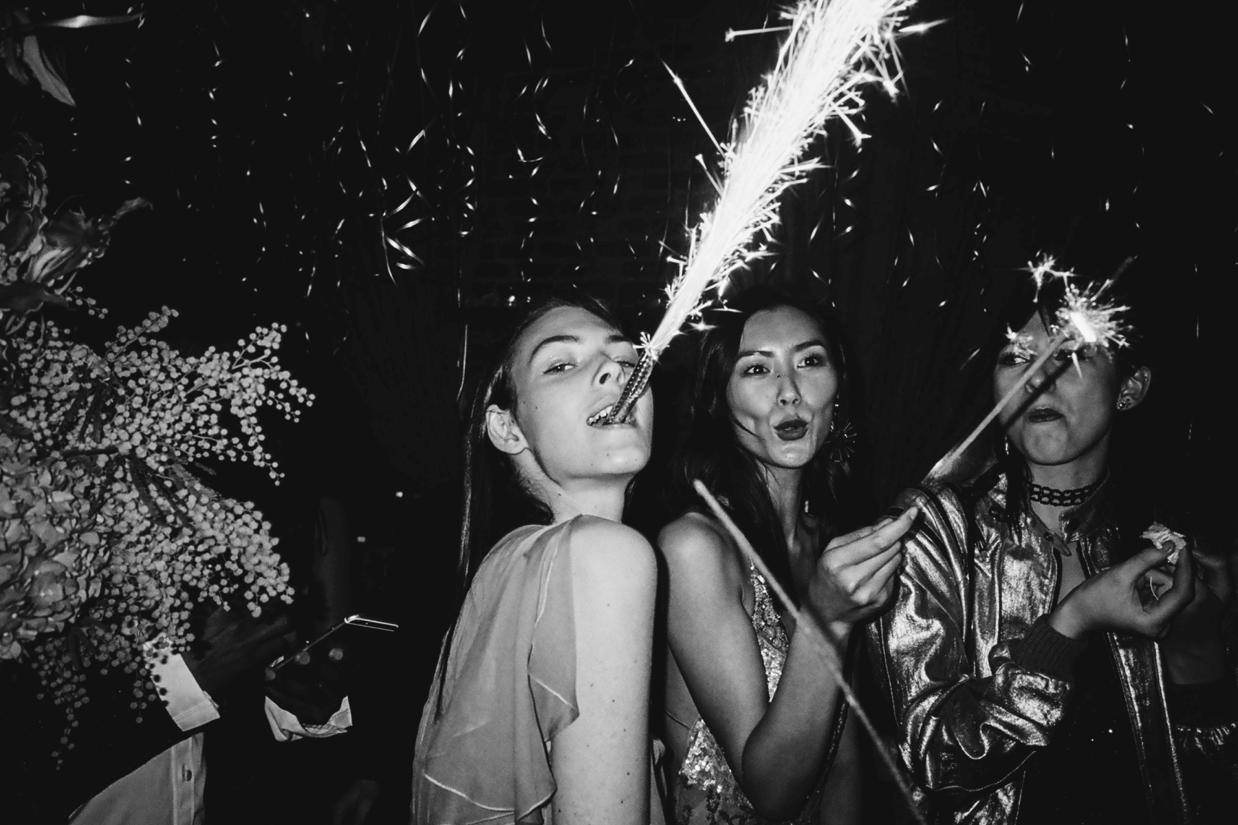 A black and white imsge of three women with celebratory sparklers.