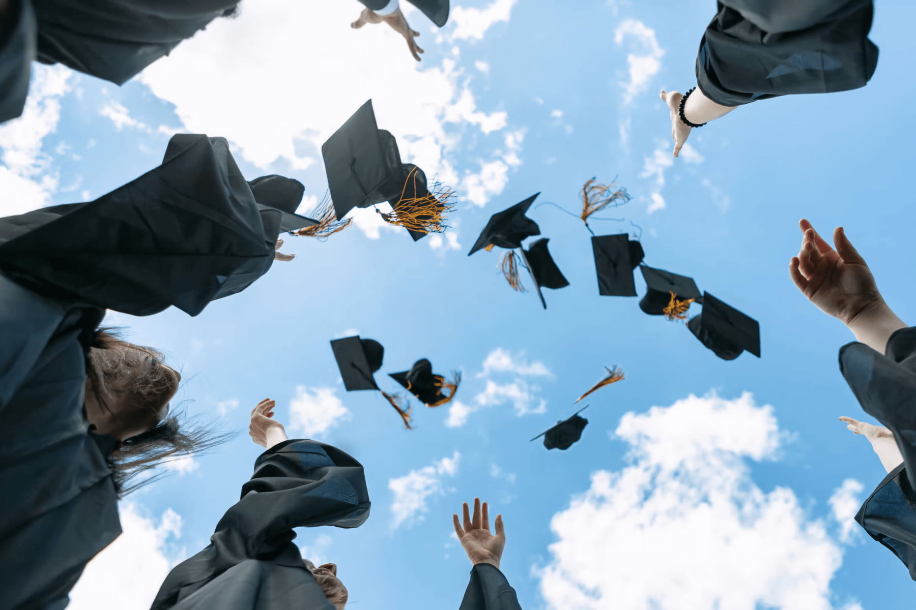Graduation caps are tossed into a blue sky.