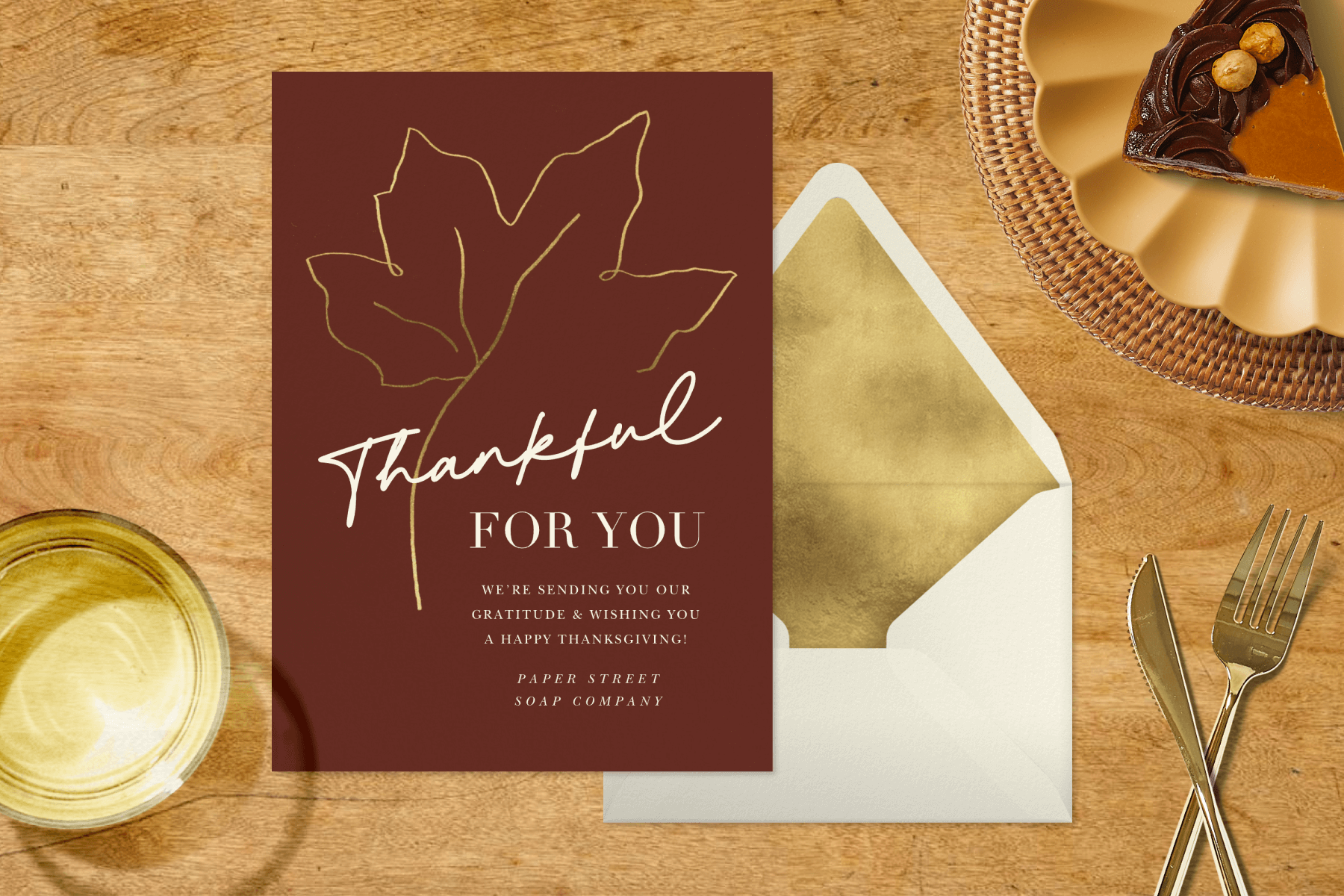 A brown thanksgiving greeting card with the words “Thankful for you.” It is surrounded by party items like a cup and a piece of pie on a plate.