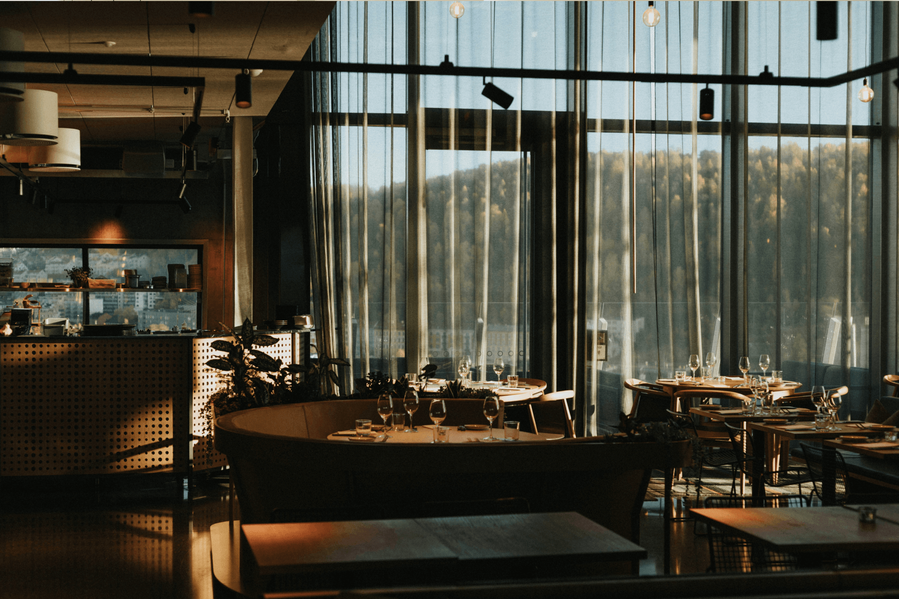 Inside a restaurant venue featuring wood booths, chairs, and tables and large glass windows.