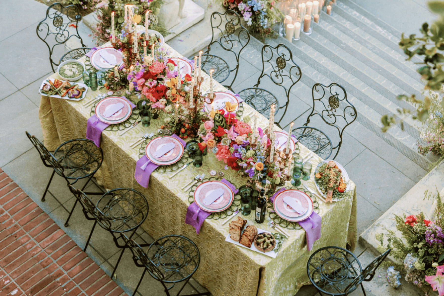 An outdoor banquet table with flowers, candles, and purple linens shown from above