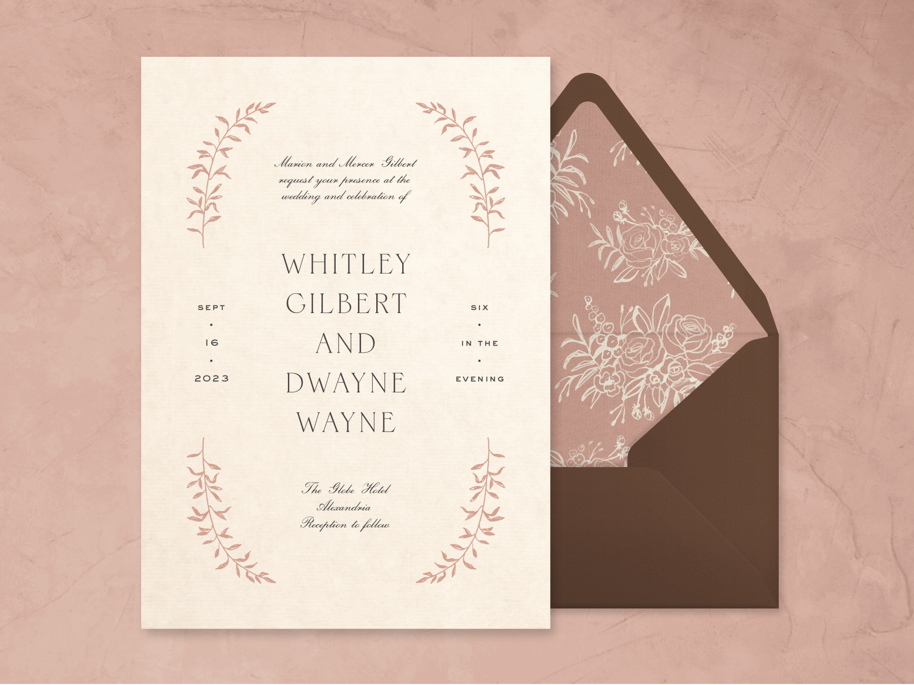 A wedding invitation with pink sprigs of leaves on each corner and a brown envelope with pink floral liner on a pink lime wash background.