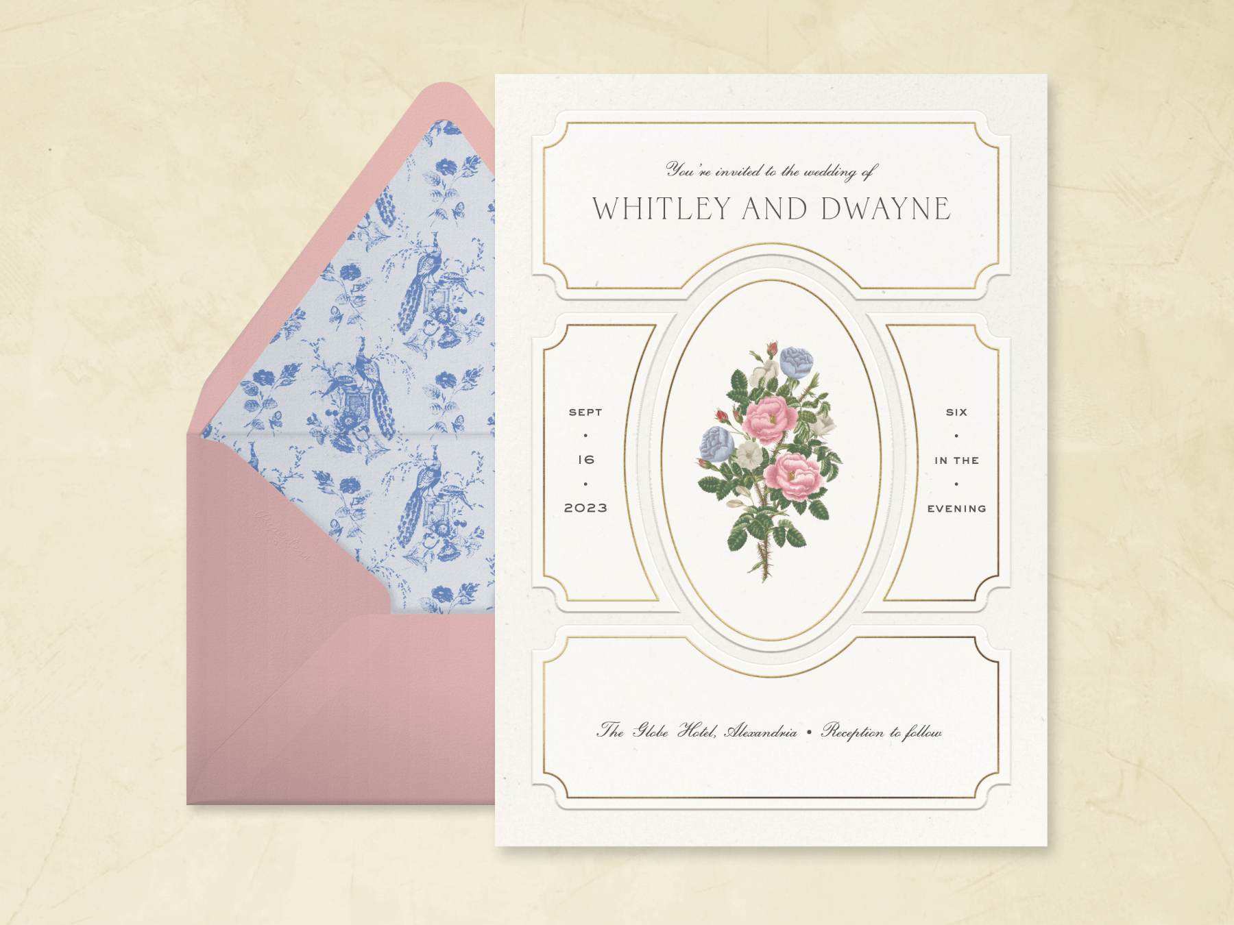 A white wedding invitation with picture frame molding-inspired shapes and an oval in the middle framing a bouquet of colorful roses and a pink envelope with a blue toile lining.
