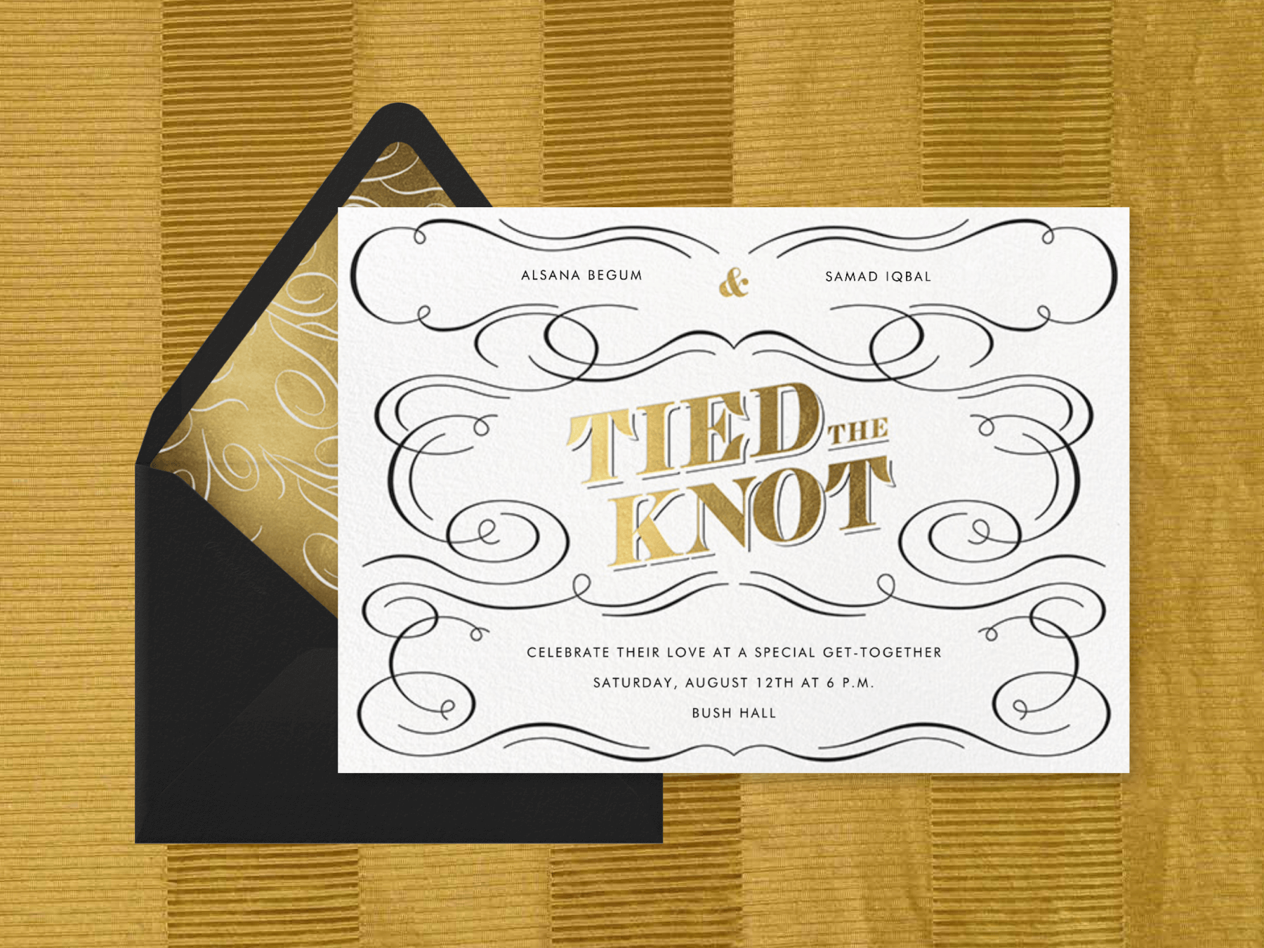 A horizontal white wedding invitation with flourish details and ornate gold lettering that reads “Tied the Knot.” It’s paired with a black envelope with a gold flourish liner.