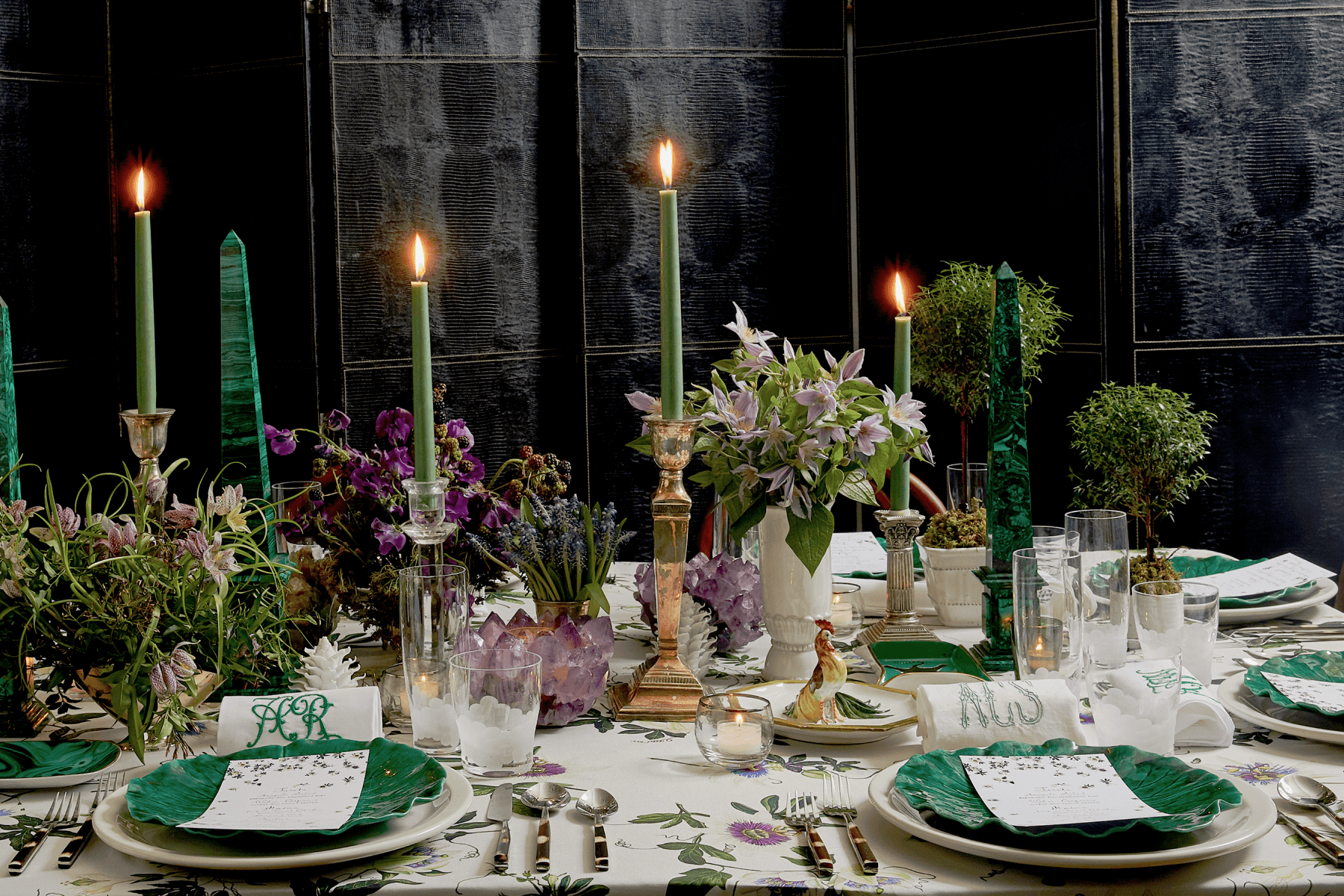 Evening, candle-lit dinner table scene with white tablecloth, green plates and purple flowers.