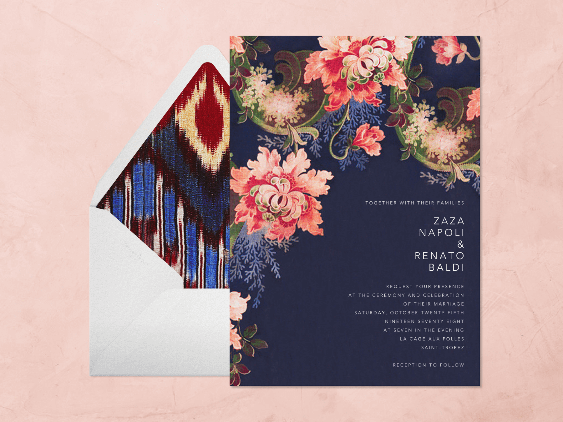 A navy blue wedding invitation with bold stylized florals creeping in from the top left corner beside a white envelope with a colorful ikat liner on a light pink background.