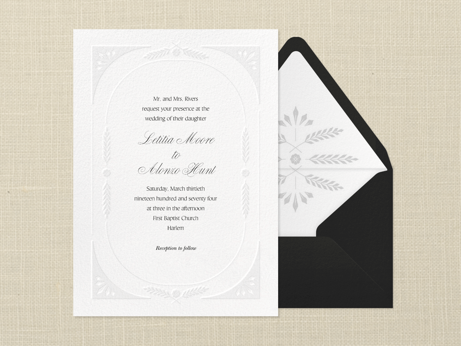 A white wedding invitation with blind embossed wheat border beside a black envelope with white liner with gray wheat sprigs and a textured neutral background.