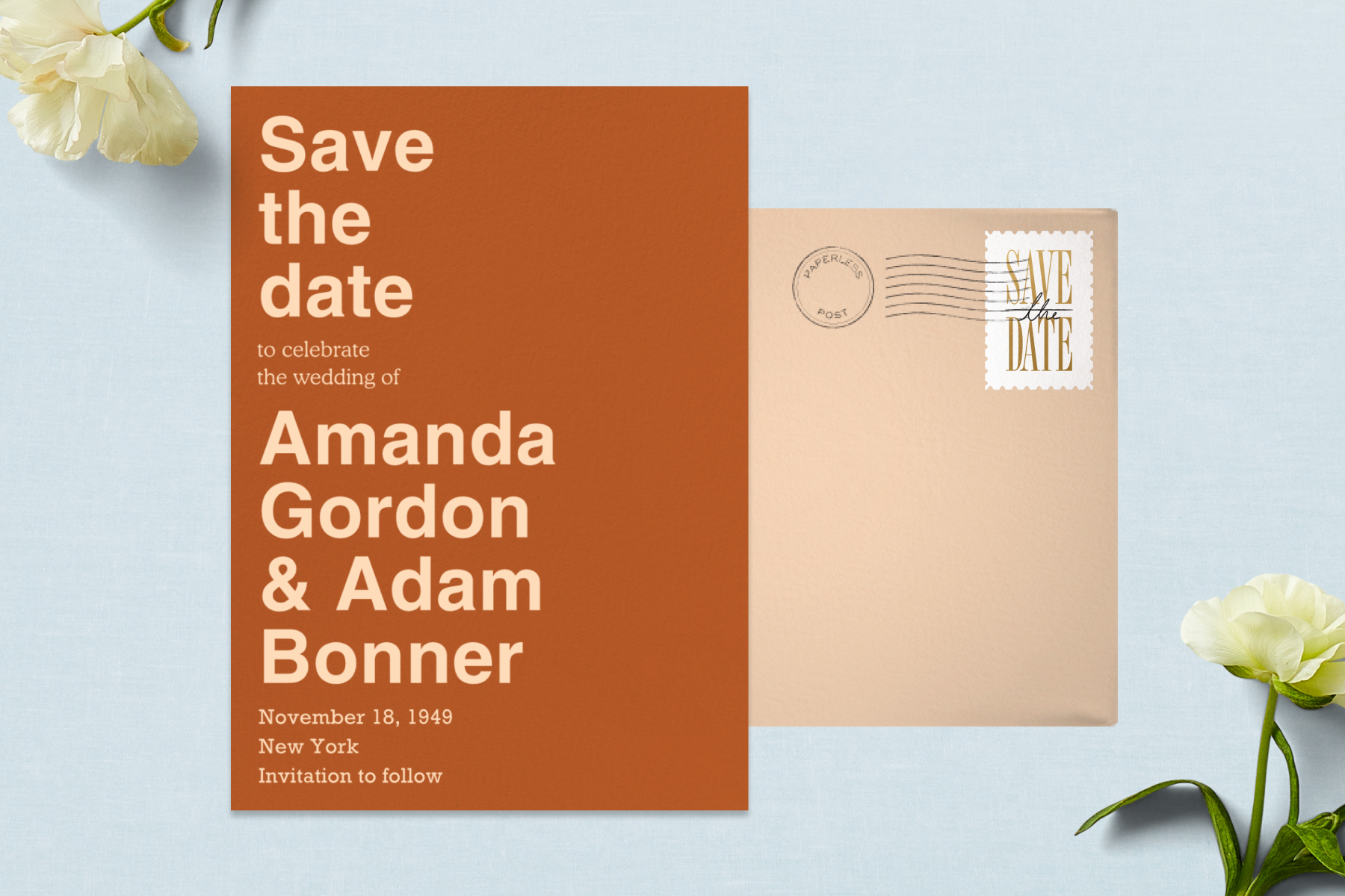 A typographical orange wedding invitation paired with a peach envelope and surrounded by white flowers.