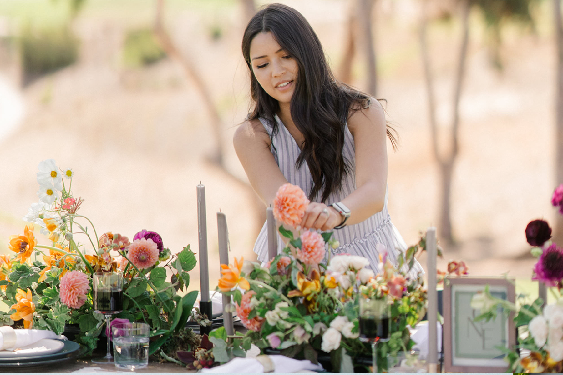 A woman arranging flower centerpieces on a long table on a warm day.