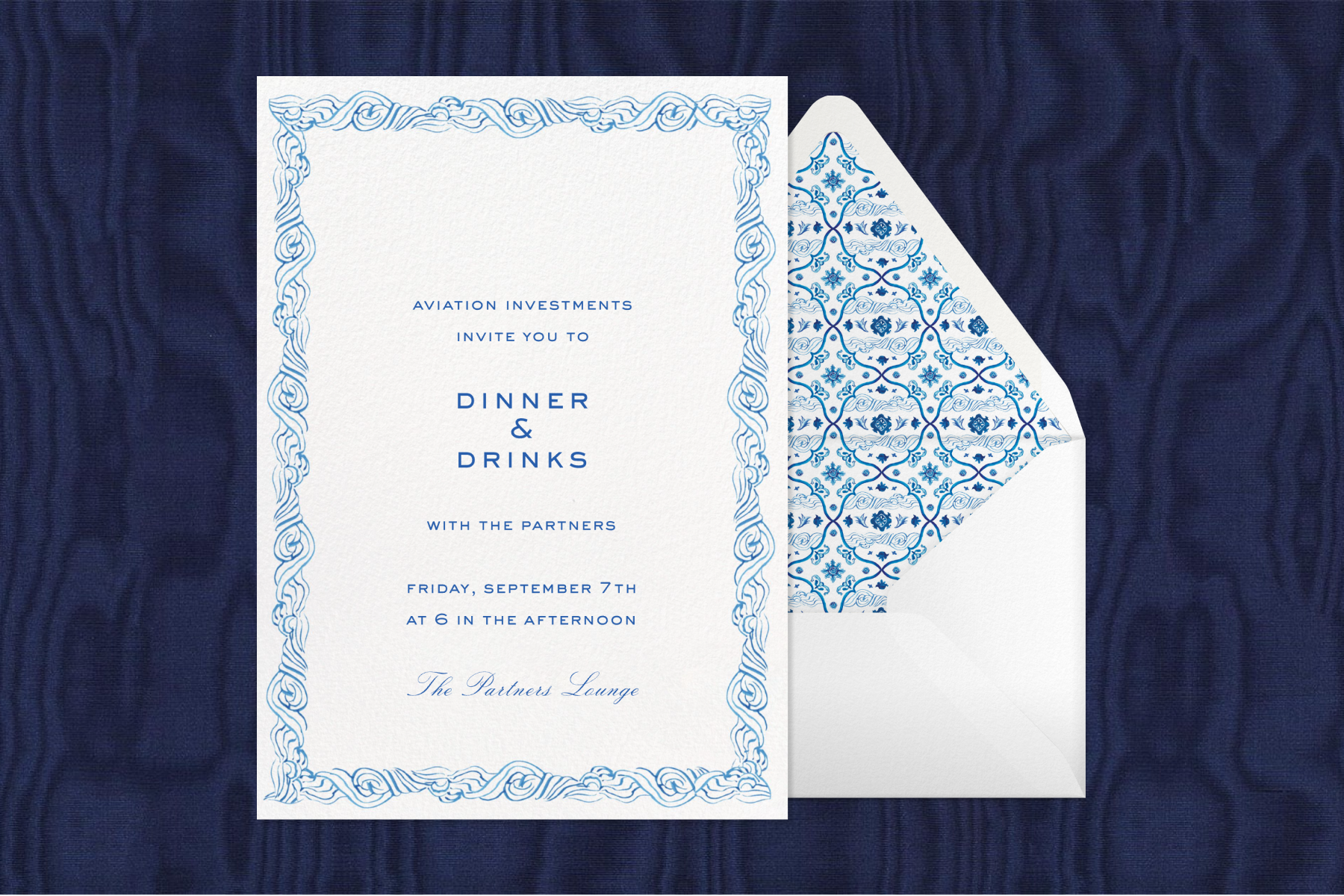 A blue and white invitation featuring text that reads ‘Dinner & Drinks’ and an illustrated patterned border paired with a white envelope, matching blue and white envelope liner, and a navy fabric background.