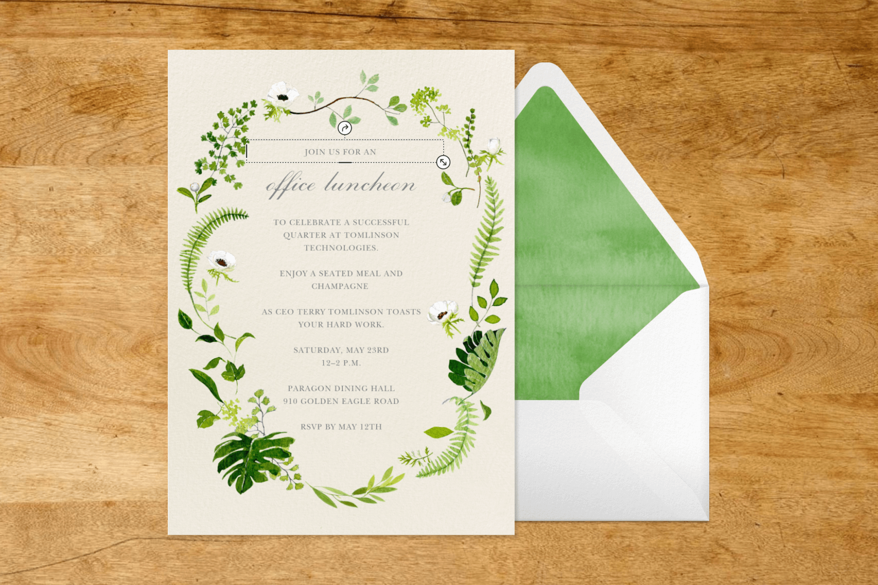 An invitation with a border of greenery and leaves beside a white and green envelope.