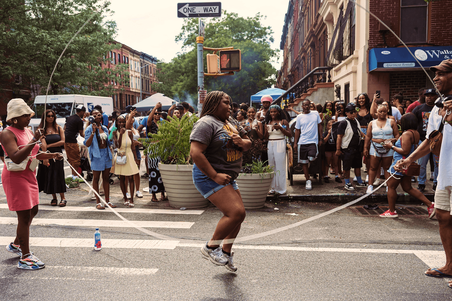  Alt text: An image of a woman double-dutching in the middle of the street as people on either side of the ropes smile in unison, with an additional crowd spectating from the sidewalk.