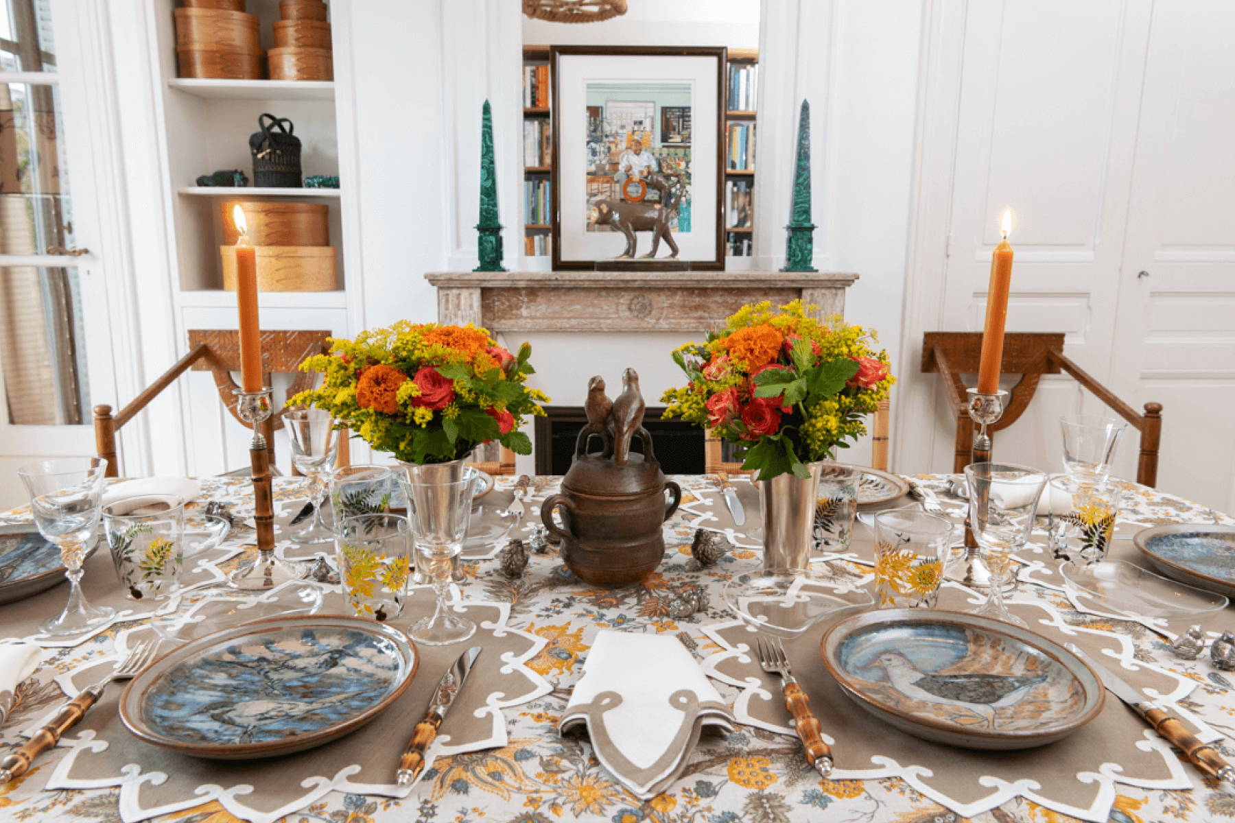 Fall-themed dinner table set with orange and yellow flower arrangements and ochre-colored candles