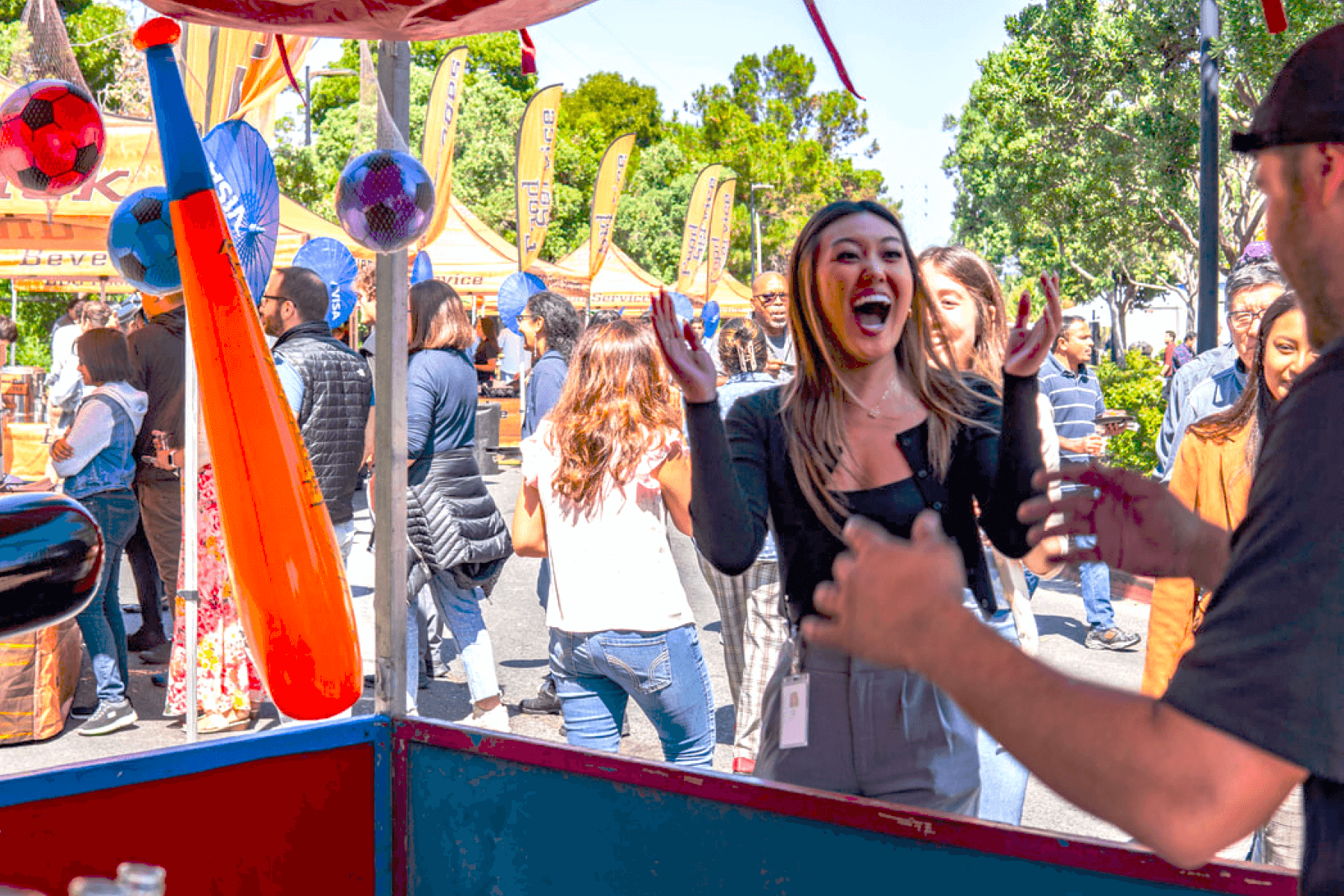 A woman waves her hands excitedly at a carnival game stand.