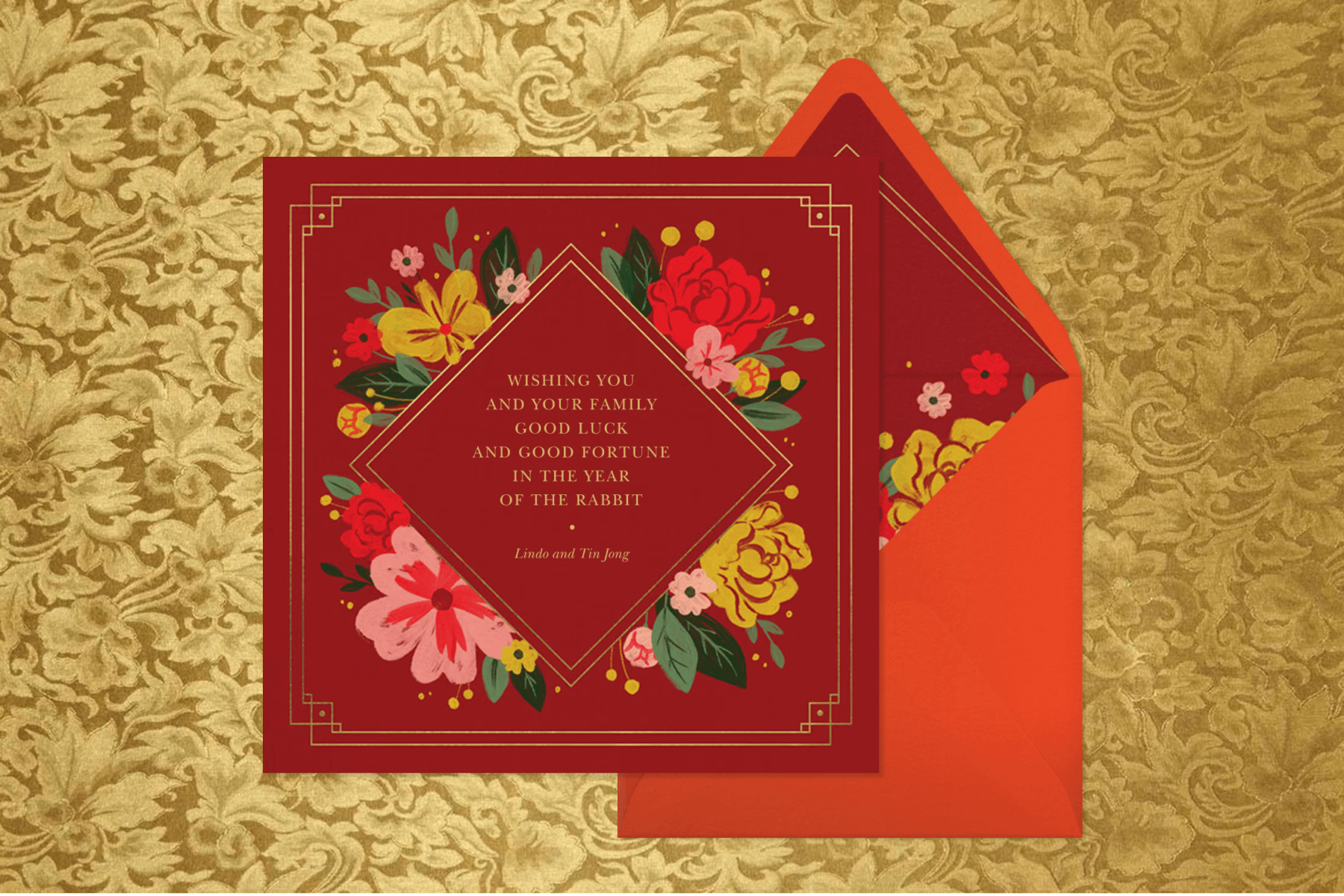 A red square invitation with delicate floral detailing and a gold edge atop a red envelope with matching liner on a gold floral backdrop. 