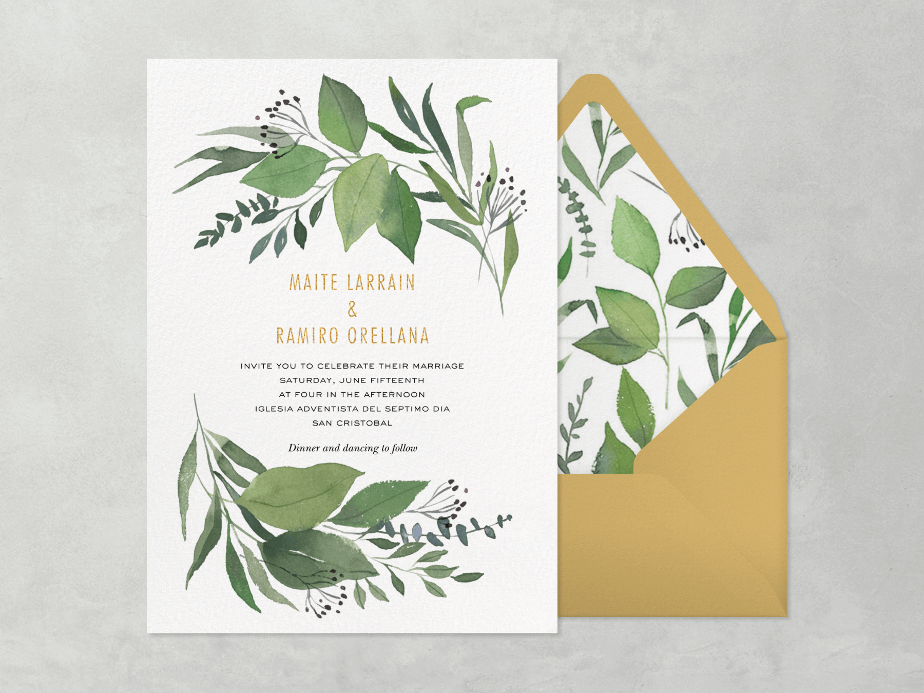 A wedding invitation with watercolor leaves and stems at the top and bottom with a gold envelope and a liner to match the invitation.