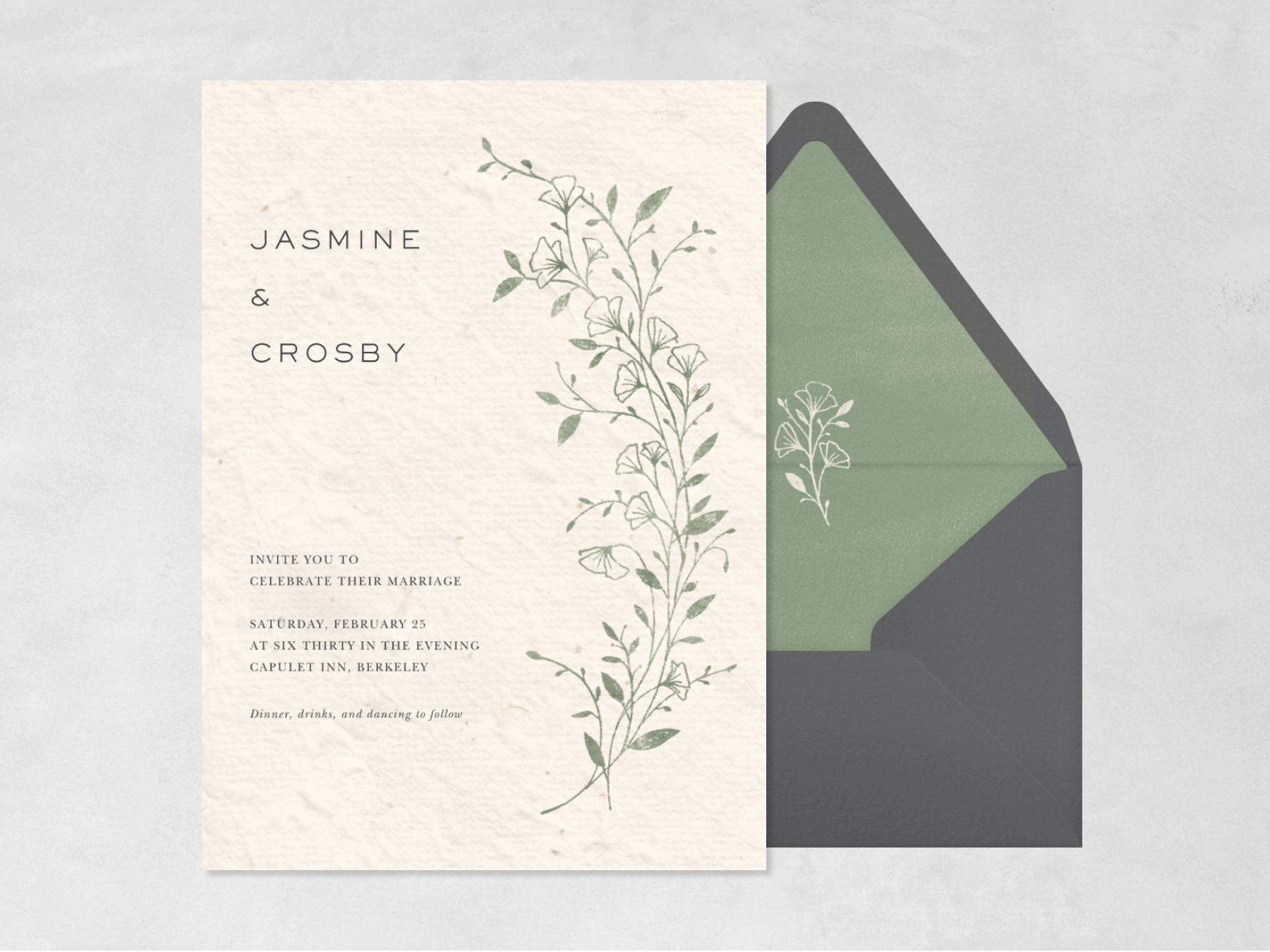 A textured cream colored wedding invitation with a delicate sage green vine with flowers on the right side, beside a gray envelope with a green liner and white sprig outlined in the center.