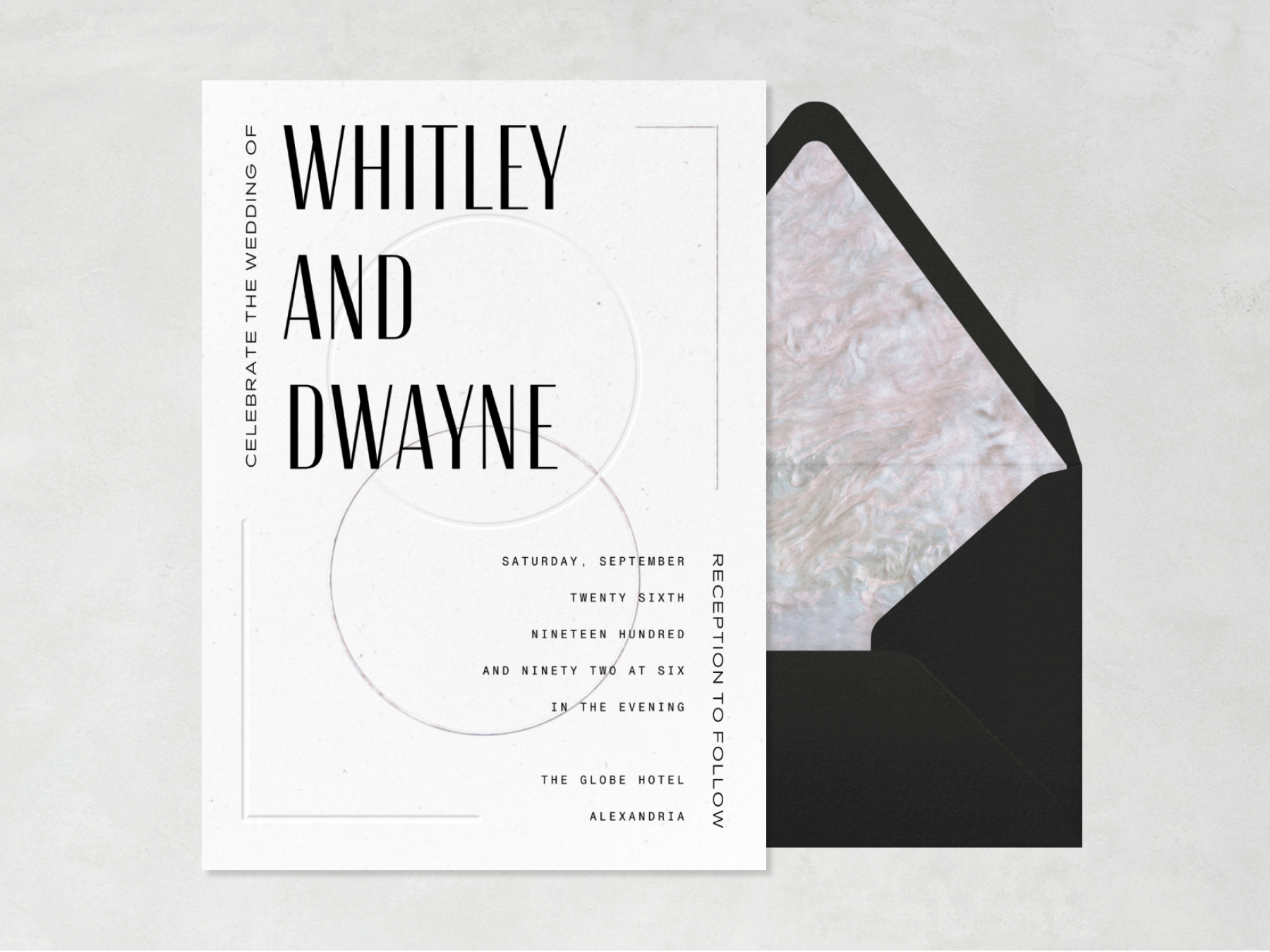 A white wedding invitation with two first names in large black lettering and thin interlocking circles beside a black envelope with marbled liner.