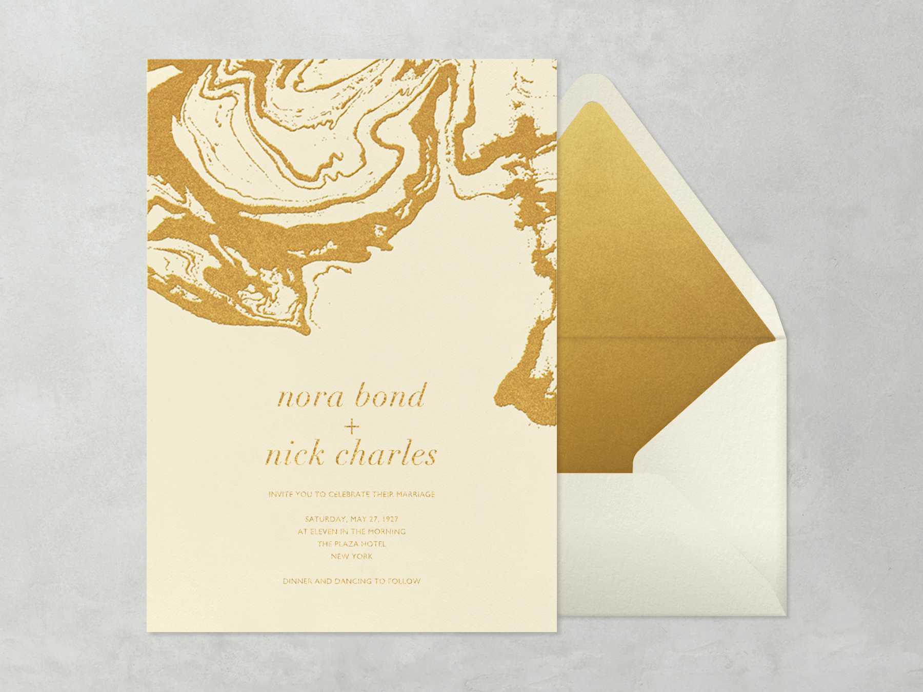 A cream wedding invitation with a gold marble effect on the top.