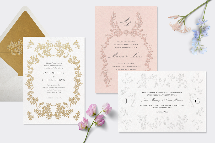 A scene with three cards: One wedding invitation with a white background and gold lace design, a pink wedding invitation with a darker pink floral design, and a white save the date card with a white lace floral design. 