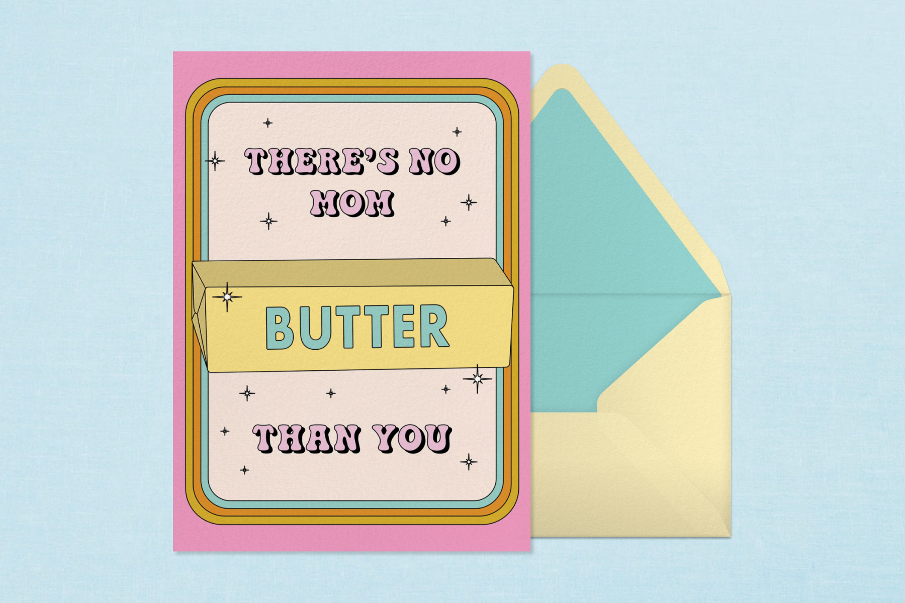 A card with a pink border that says ‘There’s No Mom Butter Than You’ with an illustration of butter in the center and sparkles surrounding the text. It sits against a yellow-and-blue envelope on a blue background.