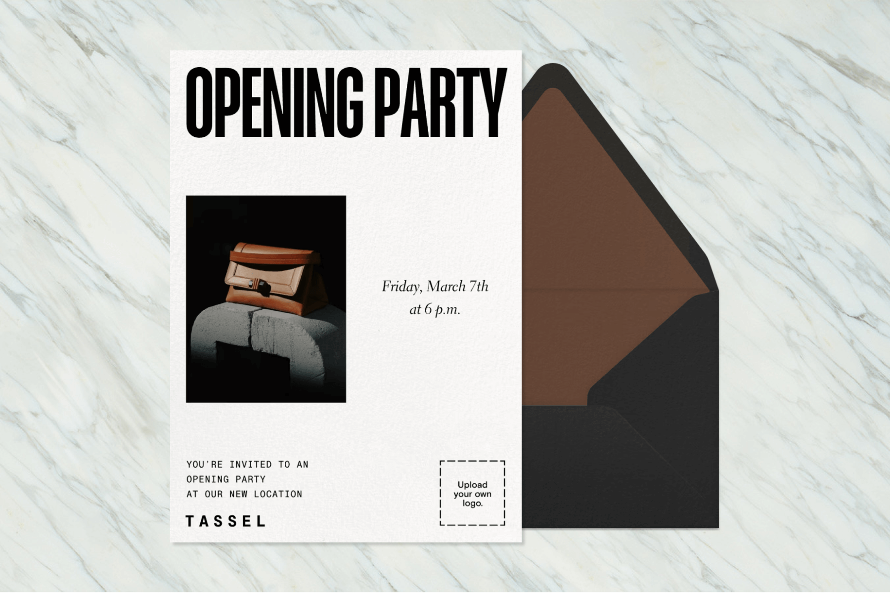 A white invitation sits on a white and gray marble background, featuring black text that reads “OPENING PARTY” with a photo of a purse, paired with a black envelope and brown envelope liner.