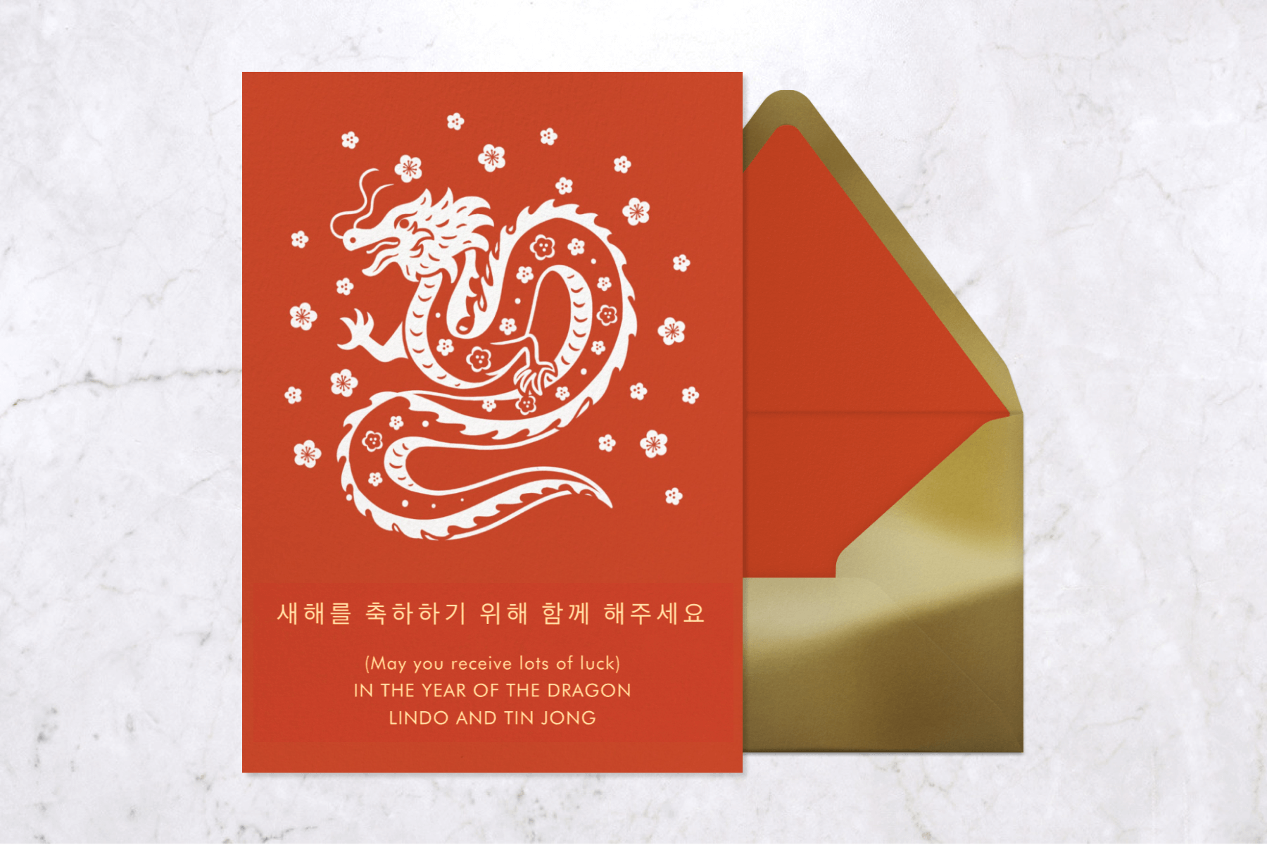 A red invitation with a white dragon and flower blossoms and gold envelope.