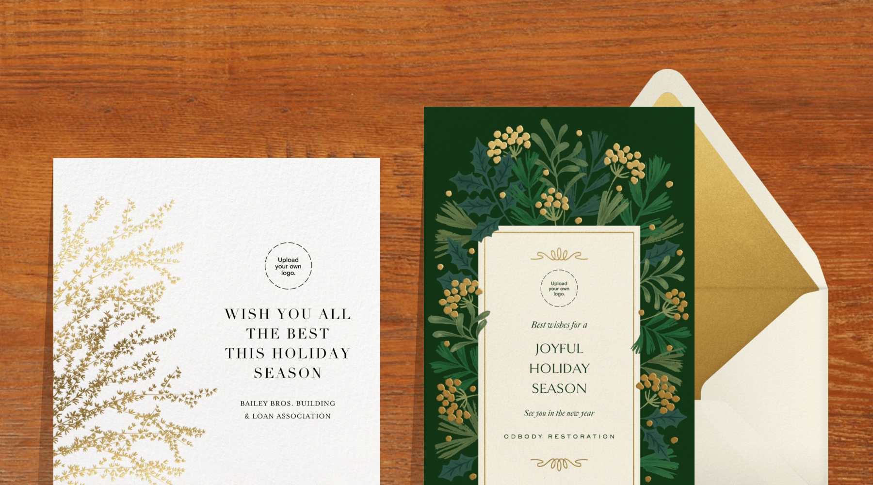 A white holiday card with gold berried branches on the side, next to a card with a dark green border with holly leaves and gold berries.